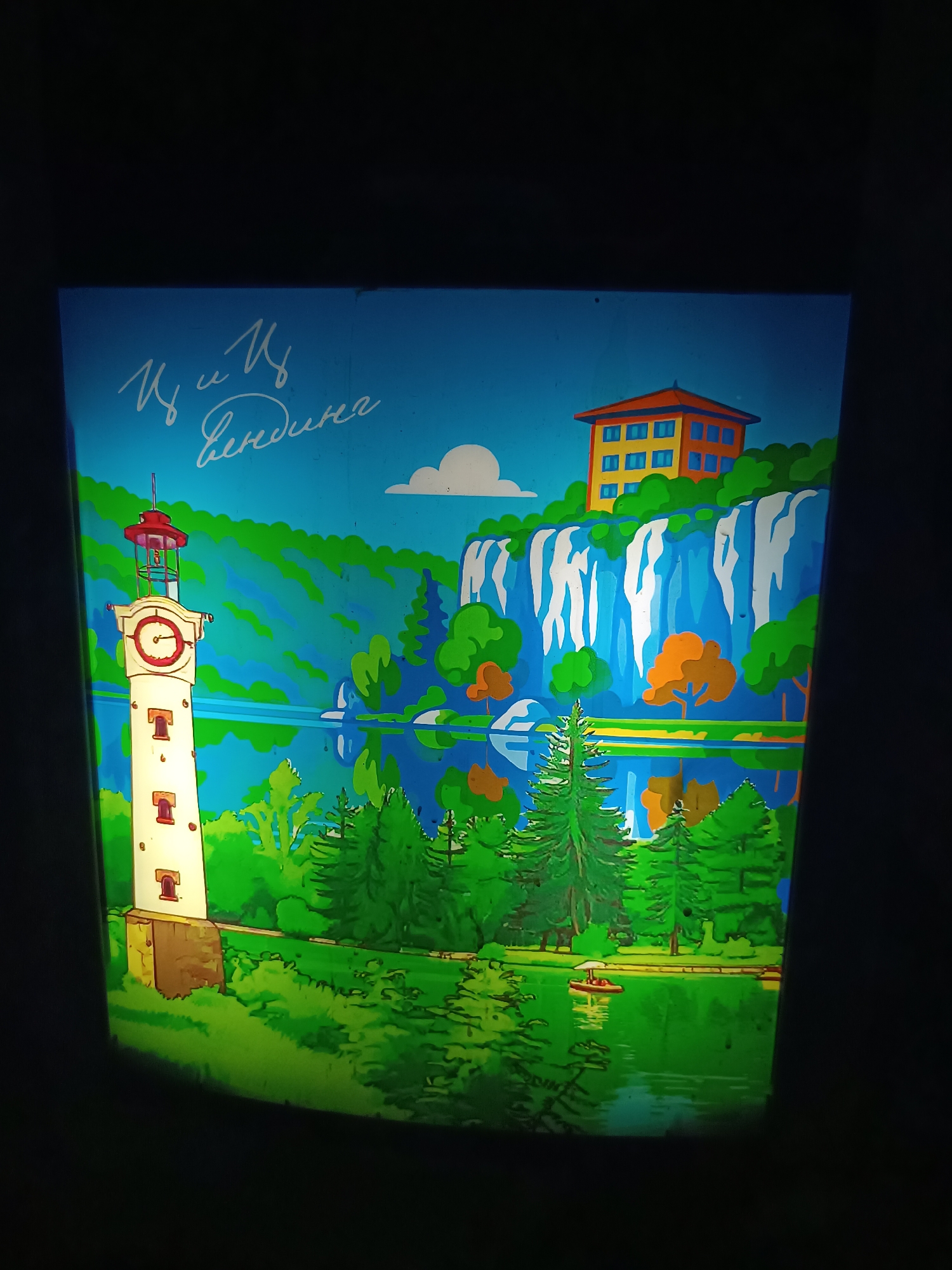 This media file is a vibrant, stylized illustration or painting, possibly a projected slide, depicting a picturesque landscape set in what is suggested to be Pleven, Bulgaria. The art style is graphic and cartoonish, utilizing bold colors and clear lines, reminiscent of vintage travel posters or children's book illustrations.
The scene features a diverse natural environment. On the left, a tall, slender white clock tower with a red conical roof and small rectangular windows stands prominently. Its clock face has red hands and markings. To the right, a multi-story yellow building with orange trim and blue windows is perched atop a green-covered cliff, overlooking the landscape. A large, multi-stream waterfall cascades down the cliff face from below this building into a serene blue lake or river that occupies the central and lower portions of the image. Lush green trees, including conifers and deciduous types, populate the hillsides and line the water's edge. One small red boat with a white canopy and two occupants is visible on the tranquil water, suggesting a recreational activity like boating.
The time of day appears to be daytime, under a clear blue sky with a single white cloud. The overall mood is peaceful and scenic. The clock tower could be a stylized representation of the Old Clock Tower of Pleven, and the natural elements like the waterfall and lake may allude to features found in Kaylaka Park or the surrounding landscapes of Pleven, Bulgaria.
In the upper left corner, there is visible handwritten text in white Cyrillic script. It reads "Ц. и Ц. Бендига" (Ts. i Ts. Bendiga), which is likely a signature from the artist or artists, or a dedication.