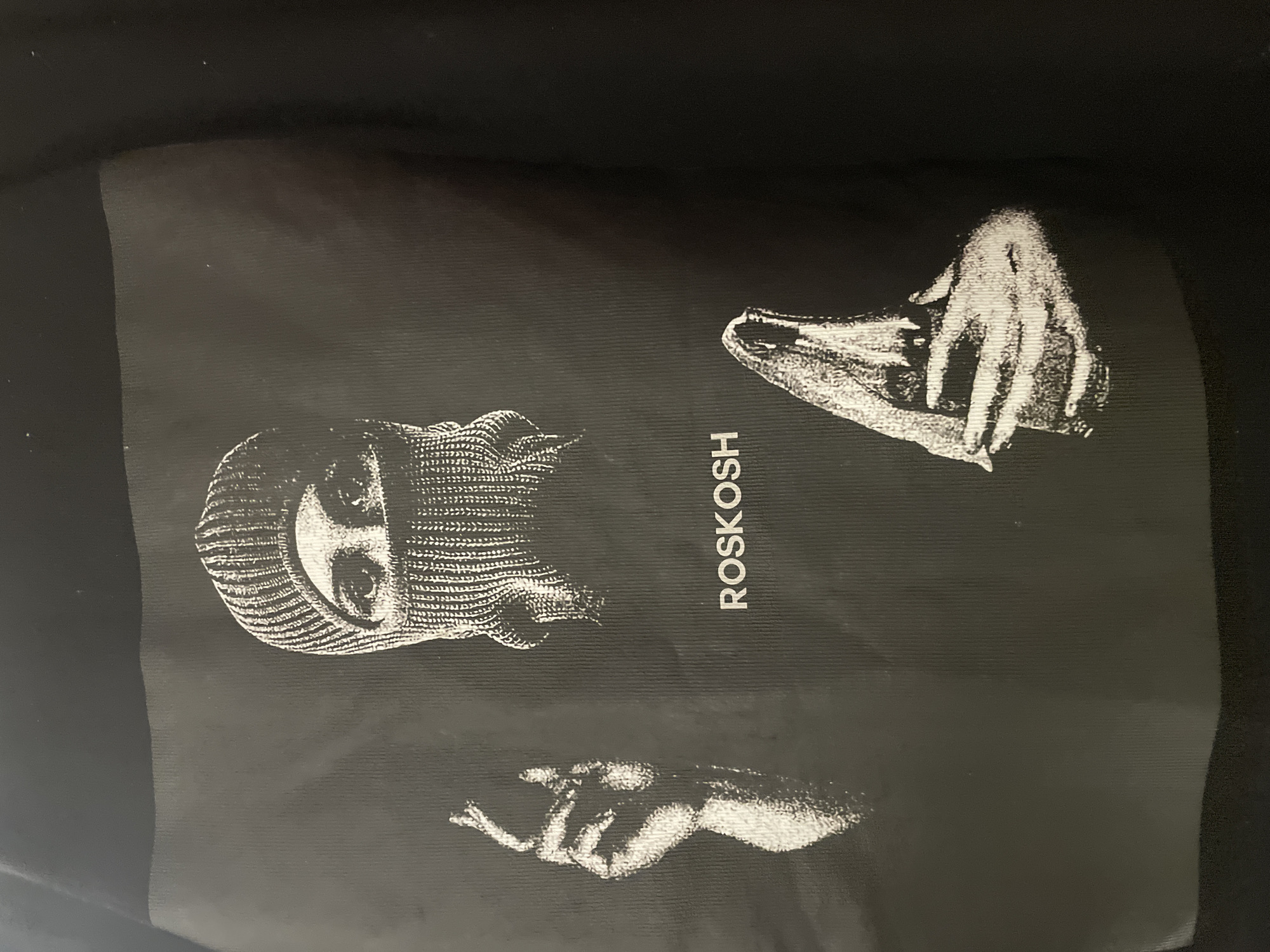 A black piece of fabric displays white printed artwork. The artwork consists of an individual wearing a ski mask, the word "ROSKOSH" vertically aligned, and two depictions of hands. The location is Unknown, Unknown.