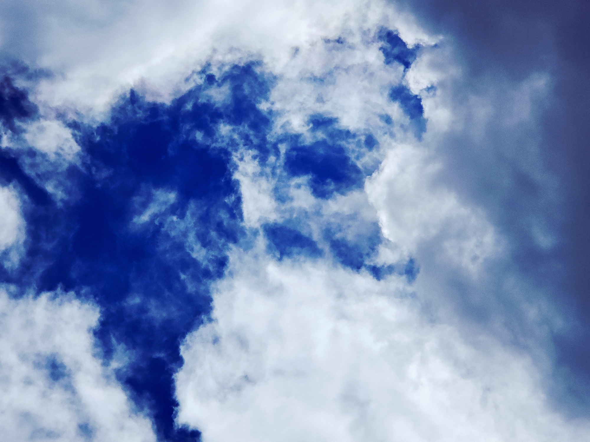 The image shows a view of the sky. The dominant colors are shades of blue and white, representing the sky and clouds. The clouds are scattered and vary in density, with some areas appearing more opaque and others more translucent. The composition is abstract in nature due to the absence of any recognizable landmarks or objects other than the sky and clouds. The location and specific actions are unknown.