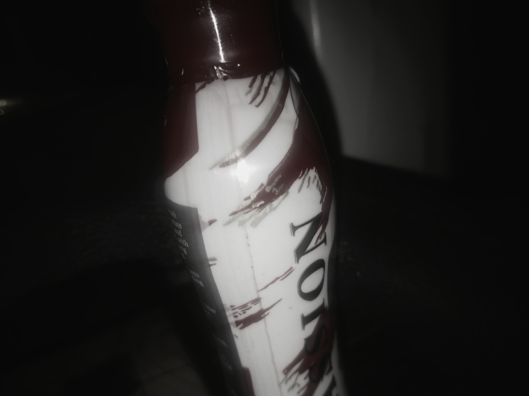 The image shows a close-up of a bottle. The bottle has a dark brown cap and a white body with dark brown markings. The word "NOT" is visible in large, bold letters on the bottle's side. There is text running vertically down the side of the bottle. Due to the limited context and the nature of the image, I cannot provide a specific location in Uyo, Nigeria, as the image does not offer any discernible location-based clues. There are no people visible.