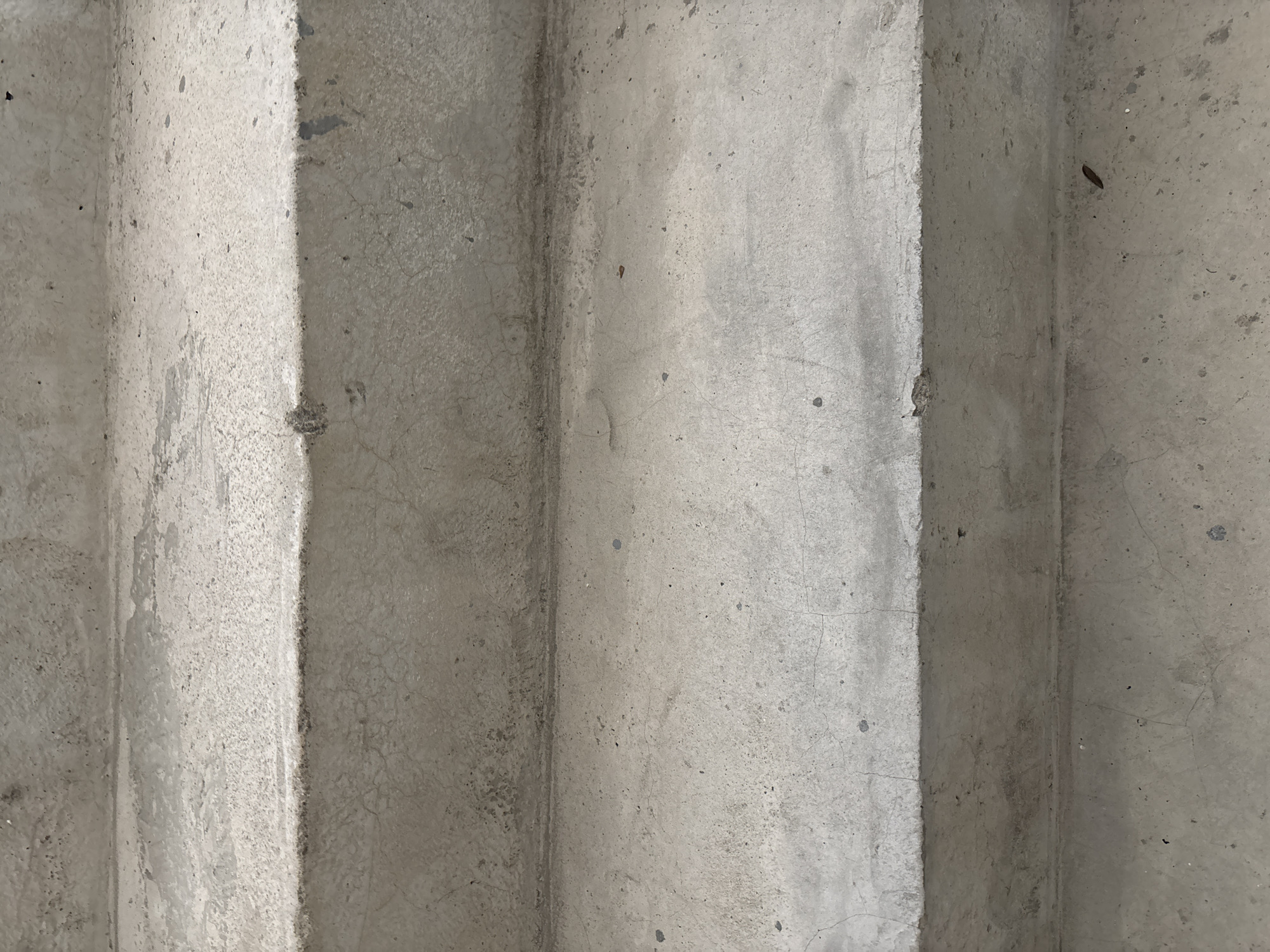 A close-up, top-down view of concrete stairs shows four distinct steps. The concrete surfaces exhibit a rough texture with visible aggregate and various imperfections such as small pits, cracks, and areas of discoloration. Some steps appear lighter than others, suggesting differences in wear or possibly remnants of water or cleaning agents. The lighting casts subtle shadows, highlighting the edges and contours of the steps, creating a sense of depth. The overall scene is devoid of any people, animals, or additional objects, presenting a stark, minimalist portrayal of utilitarian construction. The location is Unknown, Unknown.
