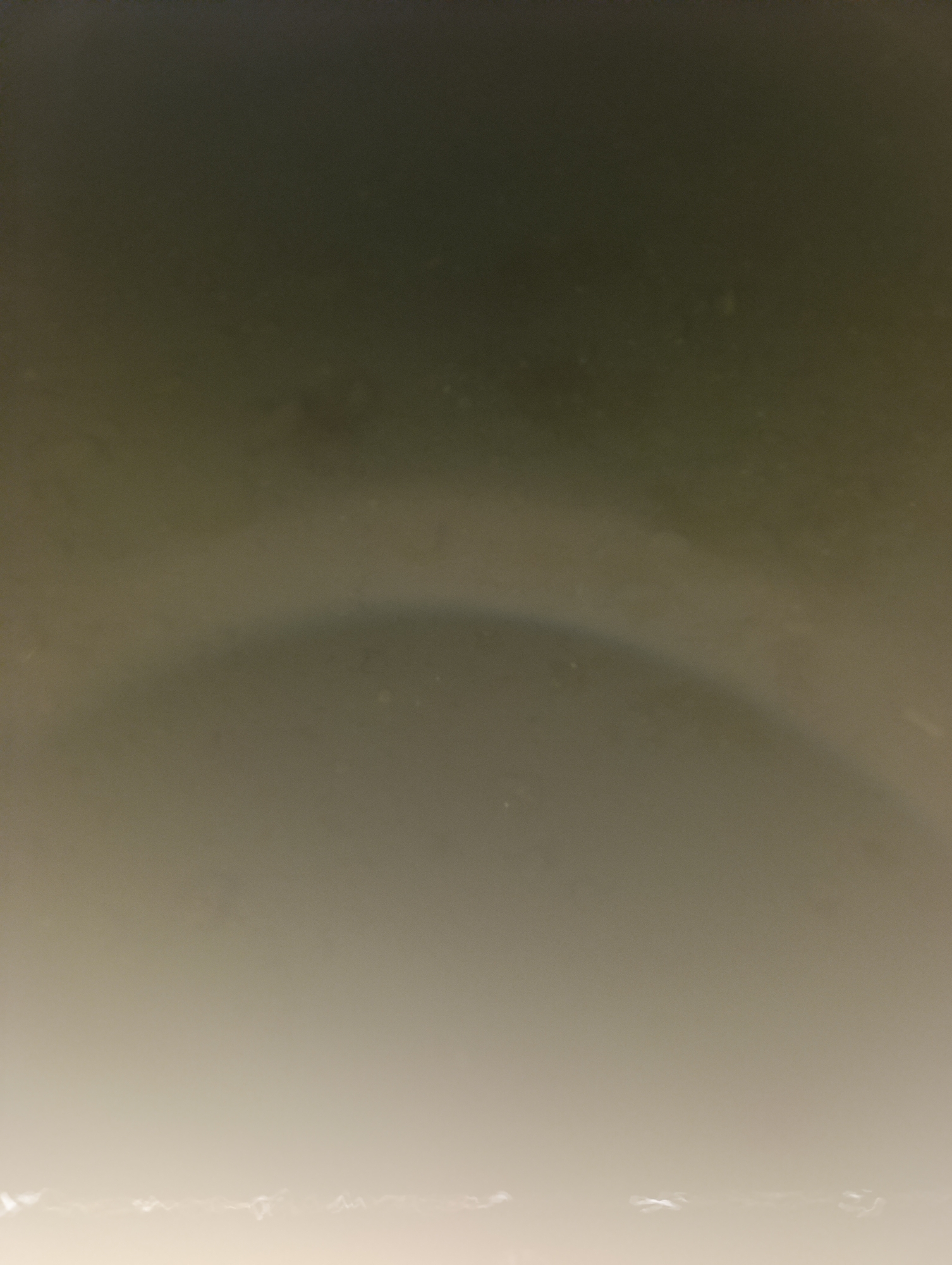 The image depicts an abstract, gradient background with varying shades of gray and beige. There is a faint, arced shadow or light band visible in the mid-section of the image, curving from left to right. The bottom portion of the image is a lighter, almost white hue, with some indistinct bright, irregular shapes. The upper portion is a darker, muted gray. The image does not contain any discernible objects, people, or actions, and therefore cannot be contextualized within a specific city or location like Bosteri, Kyrgyzstan.