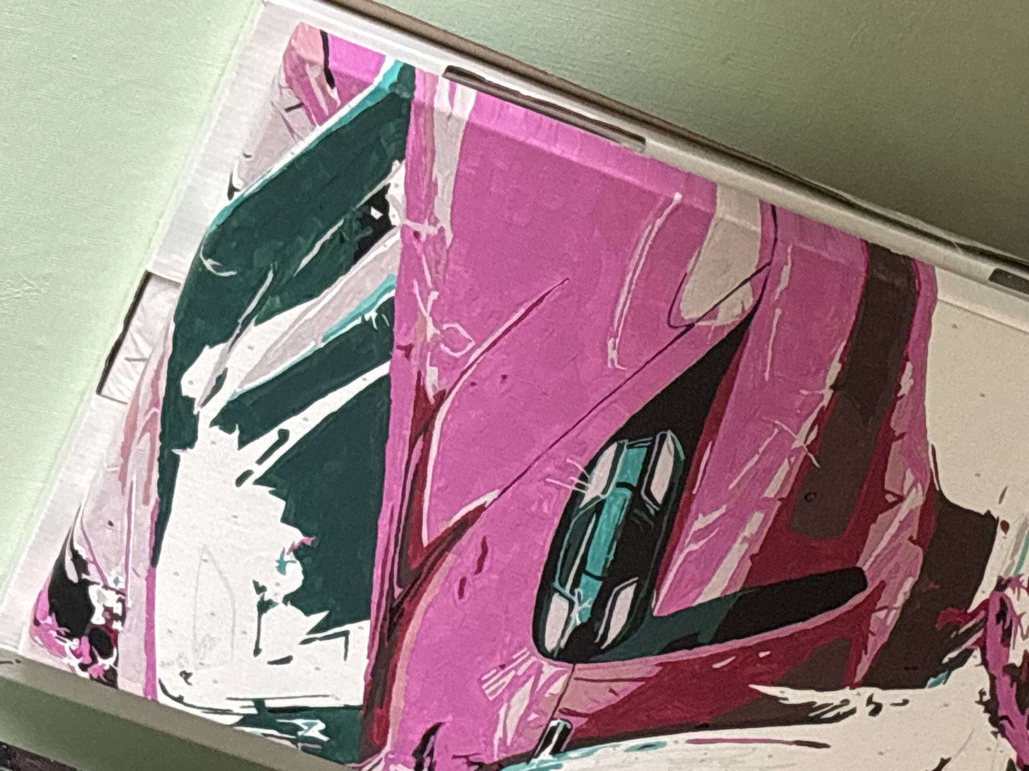 The image shows a close-up of a painting or artwork depicting a stylized car. The predominant colors are pink, green, white, and black, with accents of teal and brown. The style appears abstract or fragmented, with bold strokes and distinct color blocks. The car's cockpit area is visible, featuring what appear to be seats rendered in teal and black. The background is a light green wall. The image is a detail of the artwork, not a scene in a city. There is no relevant location and no people are involved.