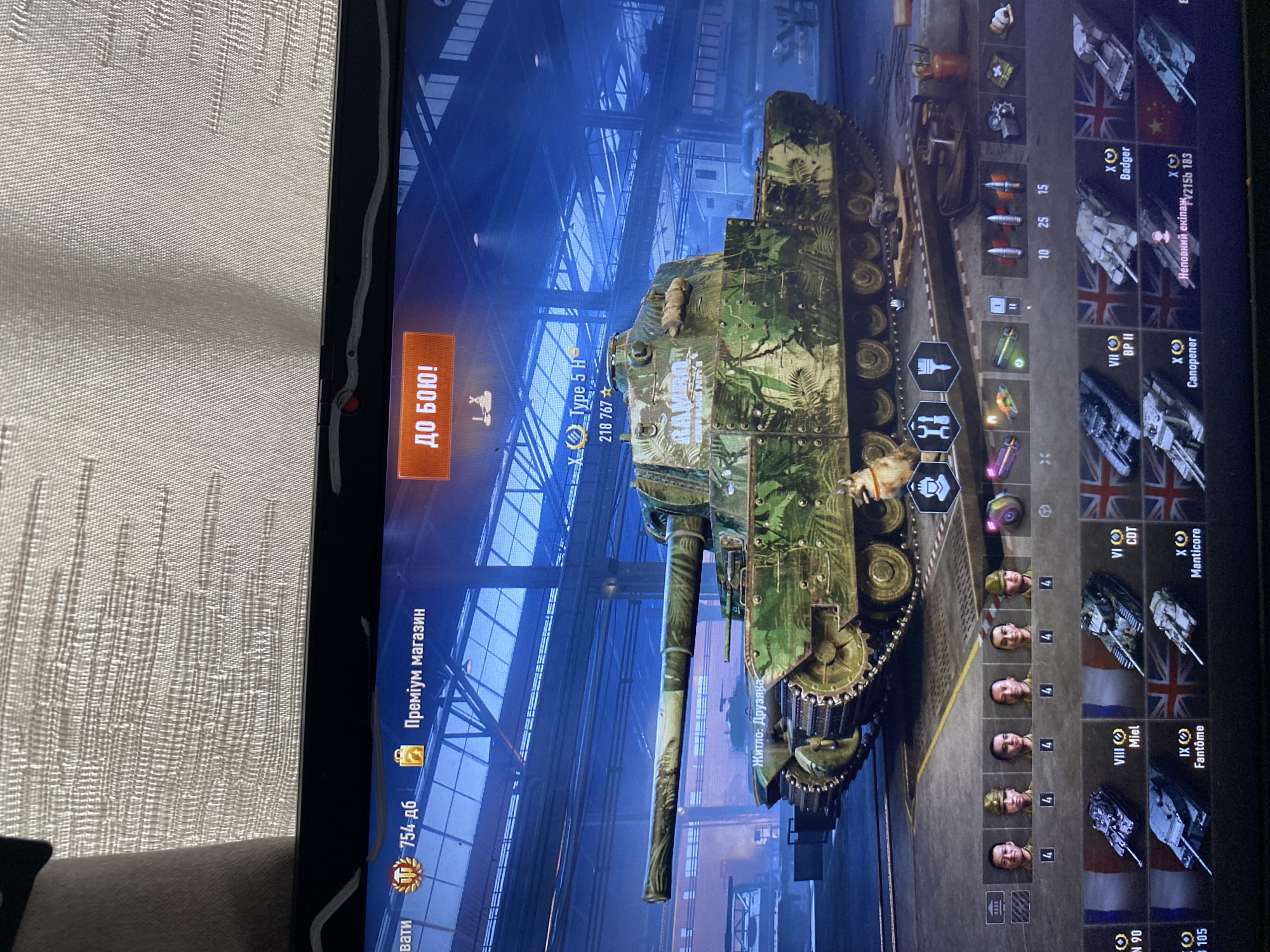 This is a screenshot of a video game, likely World of Tanks, displayed on a laptop screen. The game features a virtual tank with a camouflage pattern. The interface shows various game elements such as currency, menus, and other tanks. There is no indication of the city of Szczecin, Poland, or any real-world location within the image. The scene is entirely digital and confined to the game's virtual environment.