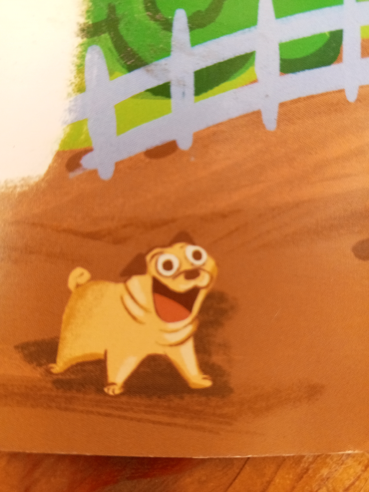 The image shows a cartoon drawing of a pug dog. The pug is light yellow and appears to be smiling with its mouth open and tongue showing. It has large, round eyes. The background of the image is a mix of brown, green, and white. There is a white fence in the upper part of the image, with green behind it. The bottom part of the image is a brown surface that could represent dirt or ground. There are shadows present on the brown surface. The image is a close-up of the pug and the immediate surroundings. There is no information in the image that would indicate its location in Chistopol, Russia.