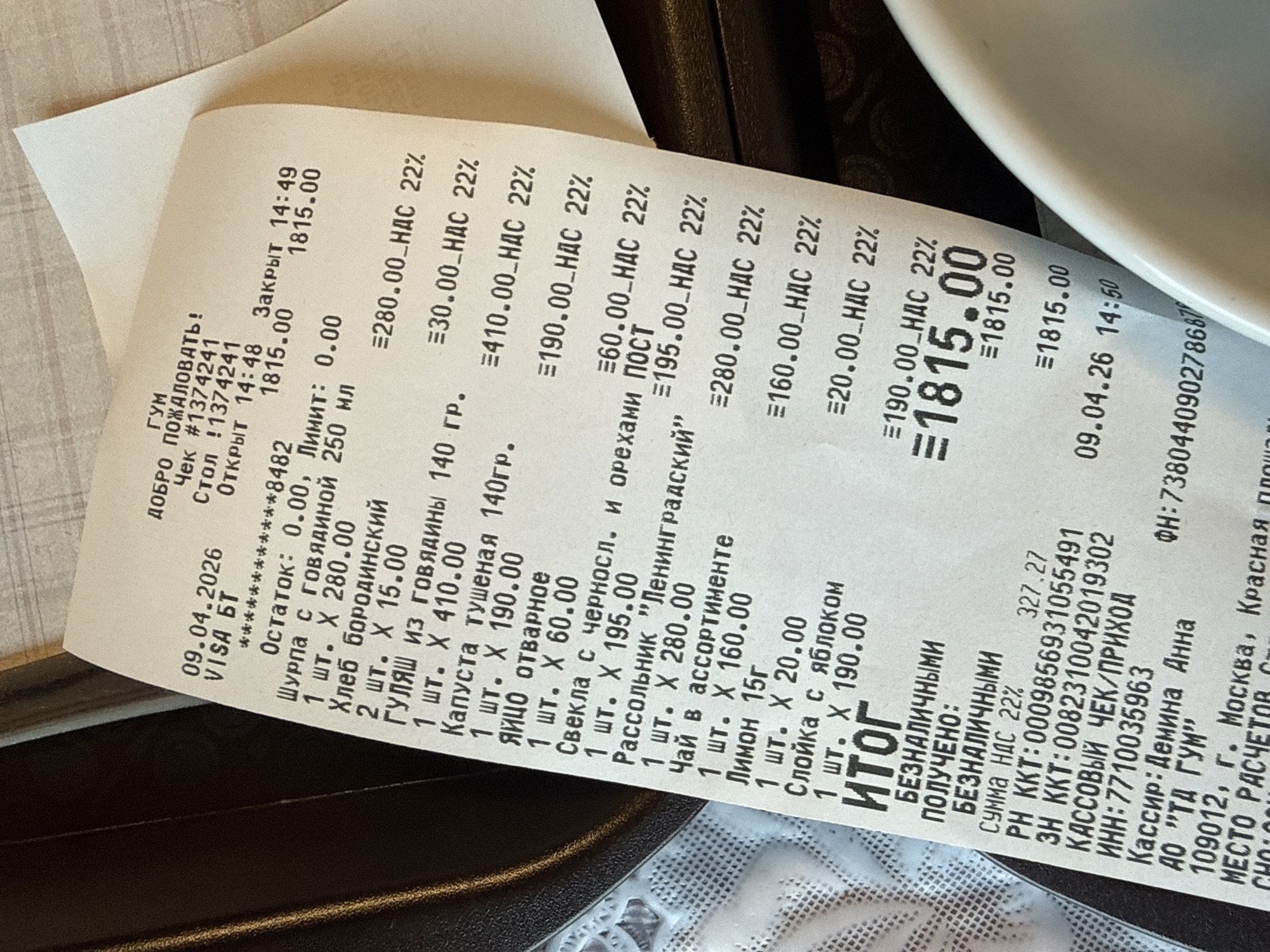 The image shows a close-up of a receipt from "ГУМ", a retail store in Moscow, Russia. The receipt is dated April 9, 2026, and indicates a purchase made with a VISA card. The receipt details a list of food items, each with its individual price and the 22% VAT (HAC). The total amount of the purchase is 1815.00, paid by cashless means. The receipt also lists the cash register information, the cashier's name (Demina Anna), and the store's address in Moscow.
