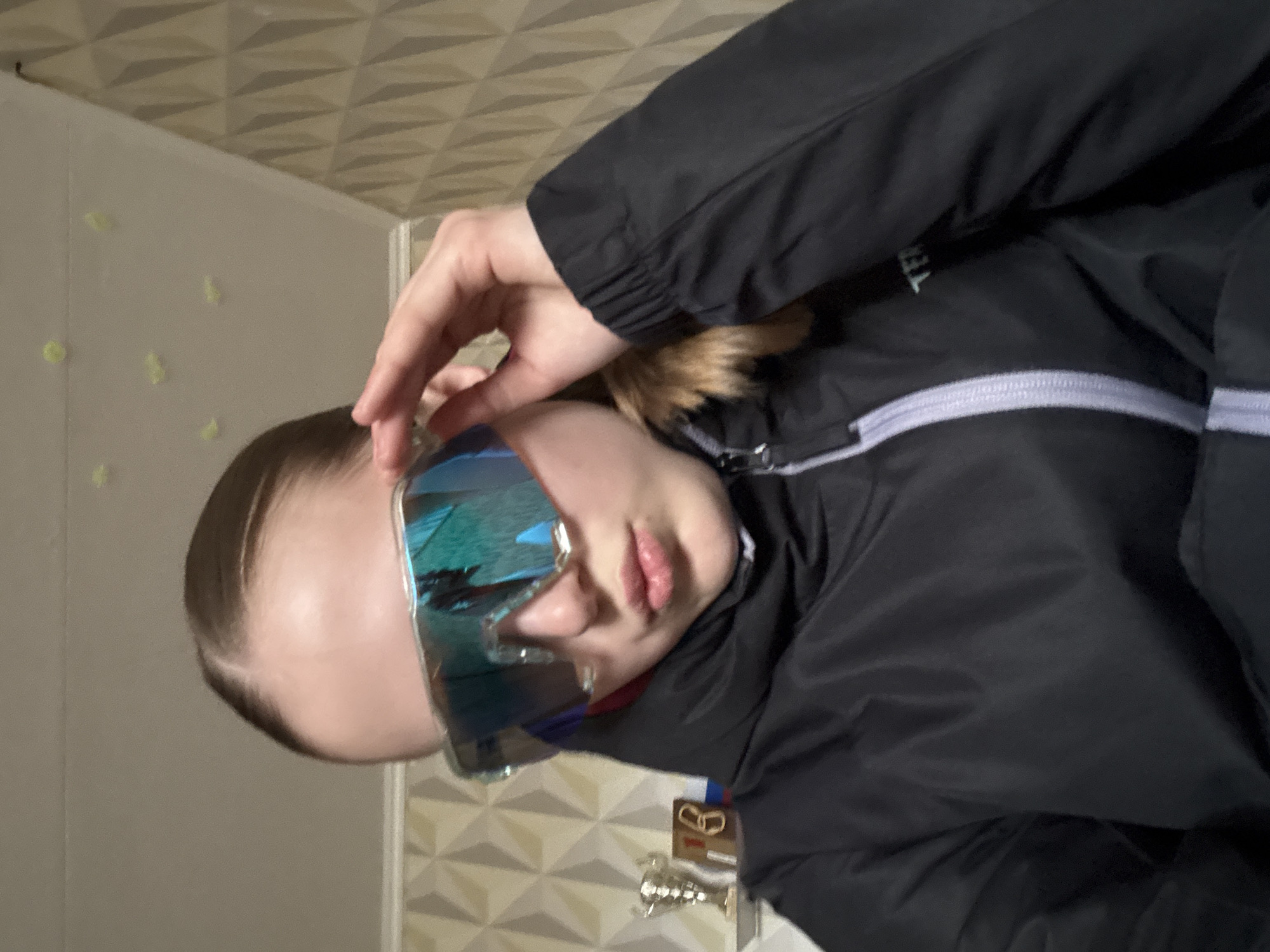 A young person wearing futuristic sunglasses and a black jacket is pictured indoors. The background includes a textured wall with geometric patterns and possibly decorative elements. Based on the metadata from the image creator, the location is Chaikovsky, Russia.