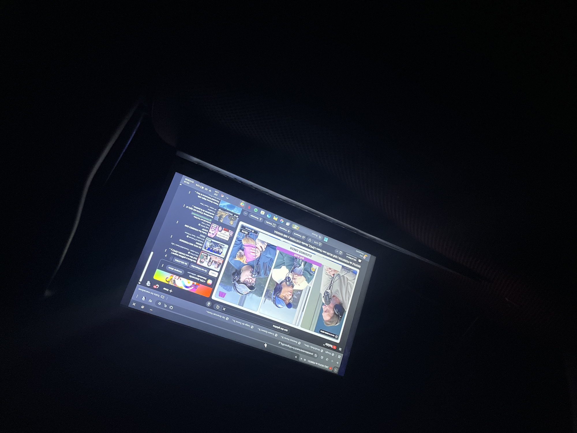 The image shows a tablet screen displaying a YouTube video titled "DESFILE de PERRITOS | QUÉ OLOR con Charo LÓPEZ, Noelia CUSTODIO y Mili GOGGIA GELATINA". The video features three individuals with headphones on, seemingly in a podcast-like setup. The YouTube interface with suggestions is visible on the left side of the screen. The tablet screen also displays a weather update from Llavallol, Argentina. The tablet is indoors, and the scene is dimly lit.