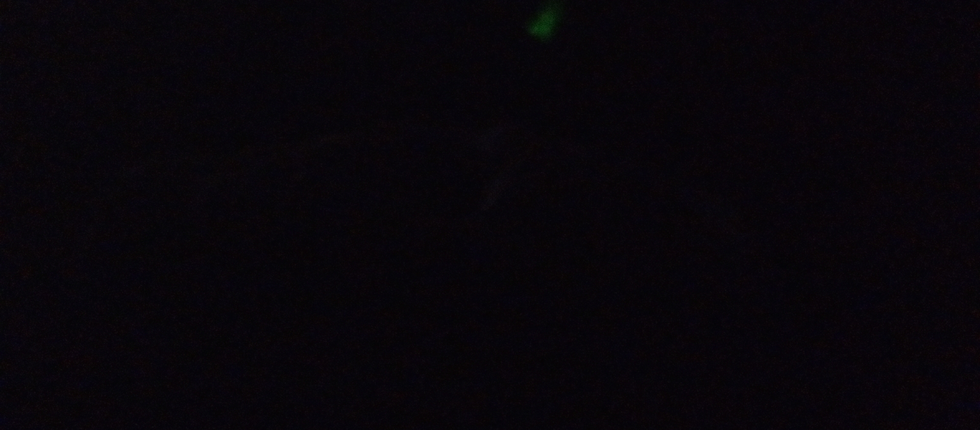 The image depicts a dimly lit, black scene with a small, blurry green object at the top center. The overall impression is of a dark environment, possibly at night or indoors with minimal lighting. No recognizable features of Nazarovo, Russia are visible. The scene is devoid of people, discernible objects, or any apparent activity.