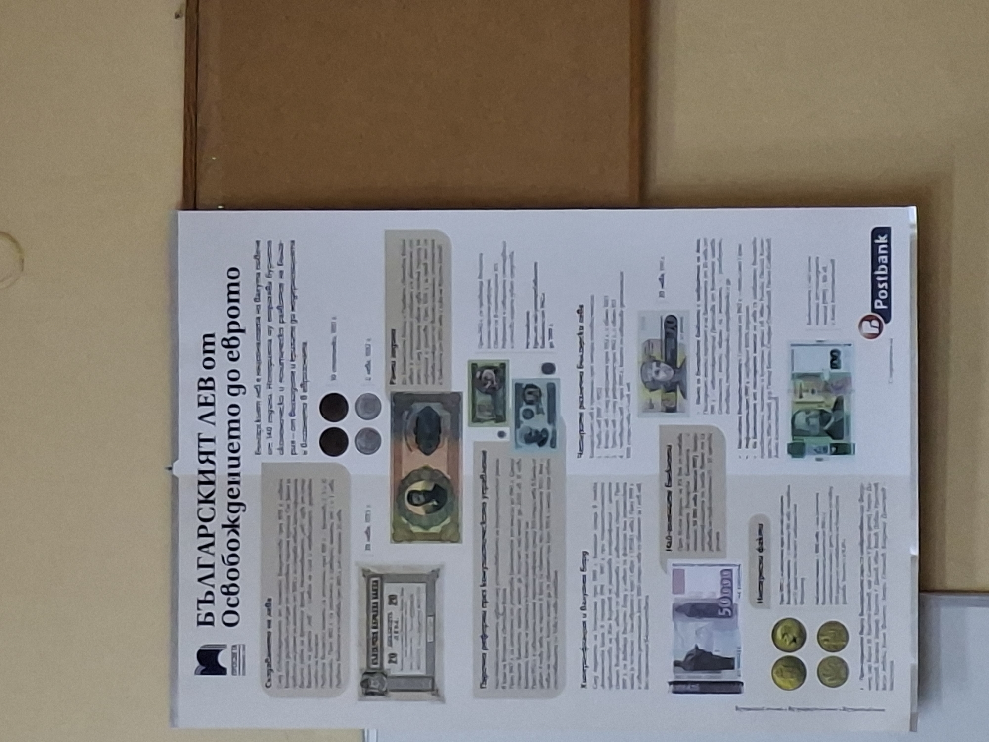 An educational display poster about the history of the Bulgarian Lev currency is presented, likely in Ruse, Bulgaria. The main subject is the evolution of Bulgarian money from the country's liberation to the potential adoption of the Euro.
The poster features the prominent title in Cyrillic: "БЪЛГАРСКИЯТ ЛЕВ от Освобождението до еврото" (THE BULGARIAN LEV from Liberation to the Euro). It is divided into several sections, each with text and illustrative images of historical and modern Bulgarian banknotes and coins. Visible currency examples include a 20 lev banknote, a 50000 lev banknote from a period of hyperinflation, and various denominations of coins (some dark, some silvery, some golden-toned).
Notable sections highlighted by text include "Парична реформа през комунистическия период" (Monetary reform during the communist period) and "Хиперинфлация" (Hyperinflation), suggesting a chronological and thematic presentation of economic history related to the currency. Another section is titled "Интересни факти" (Interesting facts).
Logos visible on the poster include "Postbank" in the top right corner and a stylized "M" or "BNB"-like logo in the bottom left, possibly representing a museum, the Bulgarian National Bank, or another cultural institution. The overall setting appears to be an indoor exhibition space, possibly a bank branch, museum, or school, with the poster pinned against a neutral-colored wall and a brown surface above it. The image is taken under artificial indoor lighting.