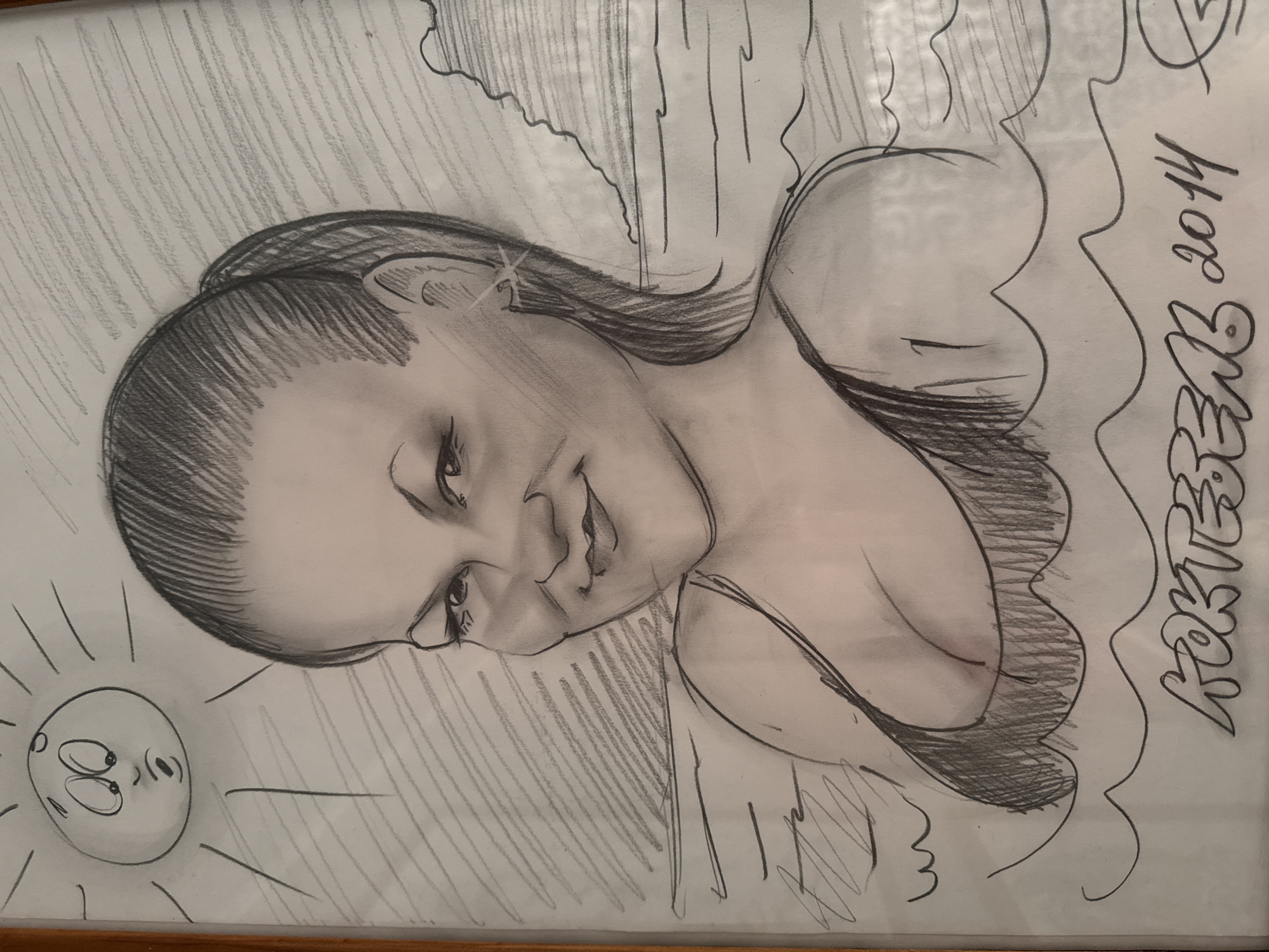 A framed graphite drawing depicts a woman's bust with a cartoonish sun in the lower left corner. The woman has dark hair pulled back, fair skin, and is wearing a top with visible cleavage. The sun has a worried expression. The background is filled with vertical and diagonal shading lines, possibly representing a wall or sky. "Korteeva 2014" is written along the right side. The drawing appears to be in a simple wooden frame. There's no indication of the location Chaikovsky, Russia in the image.