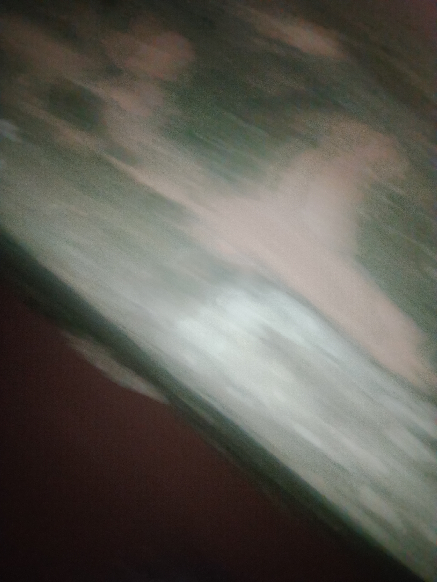 The image is an abstract, blurry photograph with diagonal streaks of light and dark colors. The dominant colors are a deep brown in the lower left, transitioning to a lighter, pale green and beige in the upper right. There are no discernible objects, people, or actions. The image's abstract nature makes it impossible to determine its location in Jalingo, Nigeria, or any other specific details about the scene.
