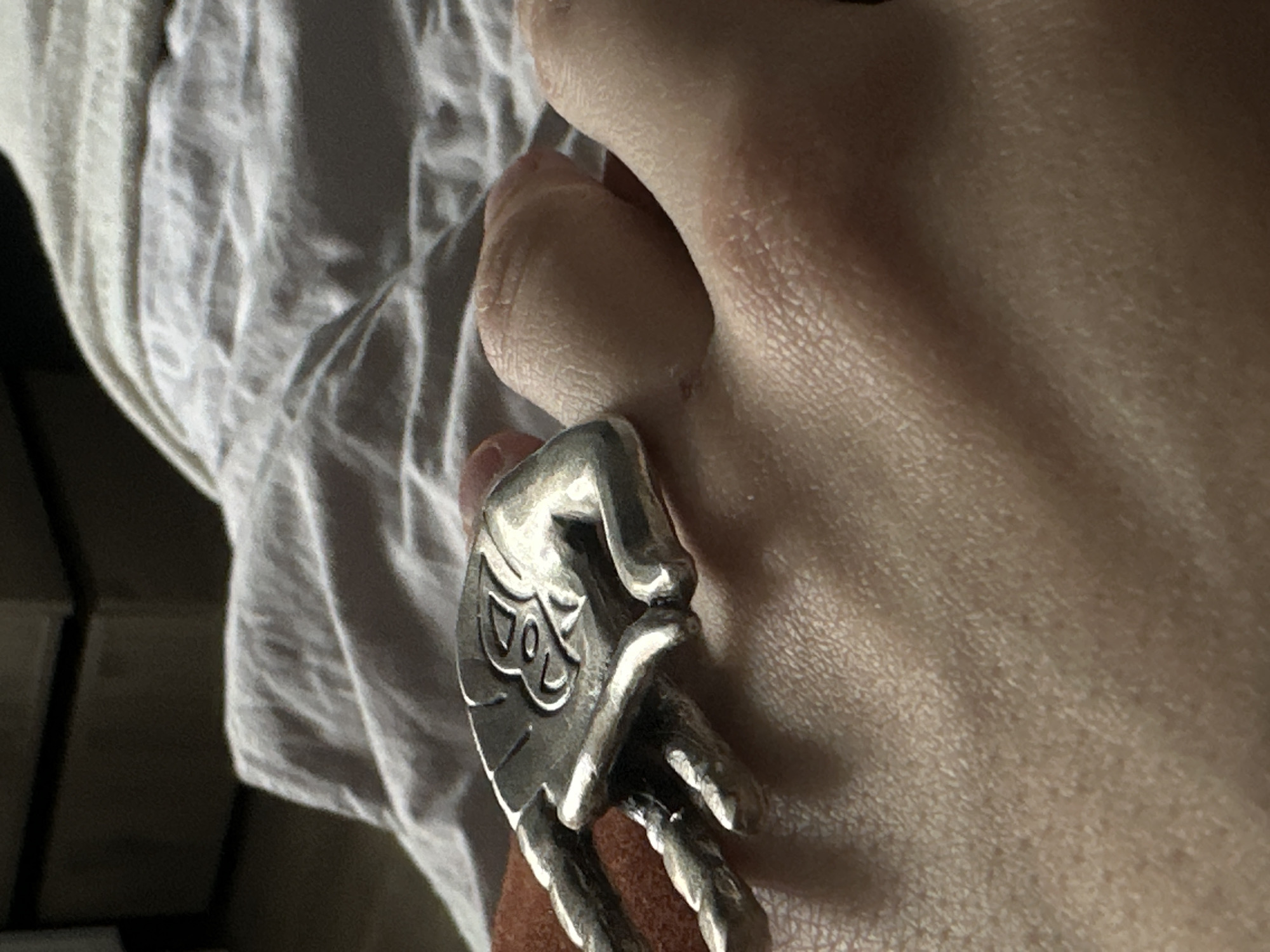 A close-up shot features a silver ring in the shape of a hand on a person's finger. The ring is detailed with etched lines and appears to be the focus of the image. The person's skin is visible, and there is a white cloth or fabric in the background. The image does not provide sufficient information to determine a location in Saint Petersburg, Russia.