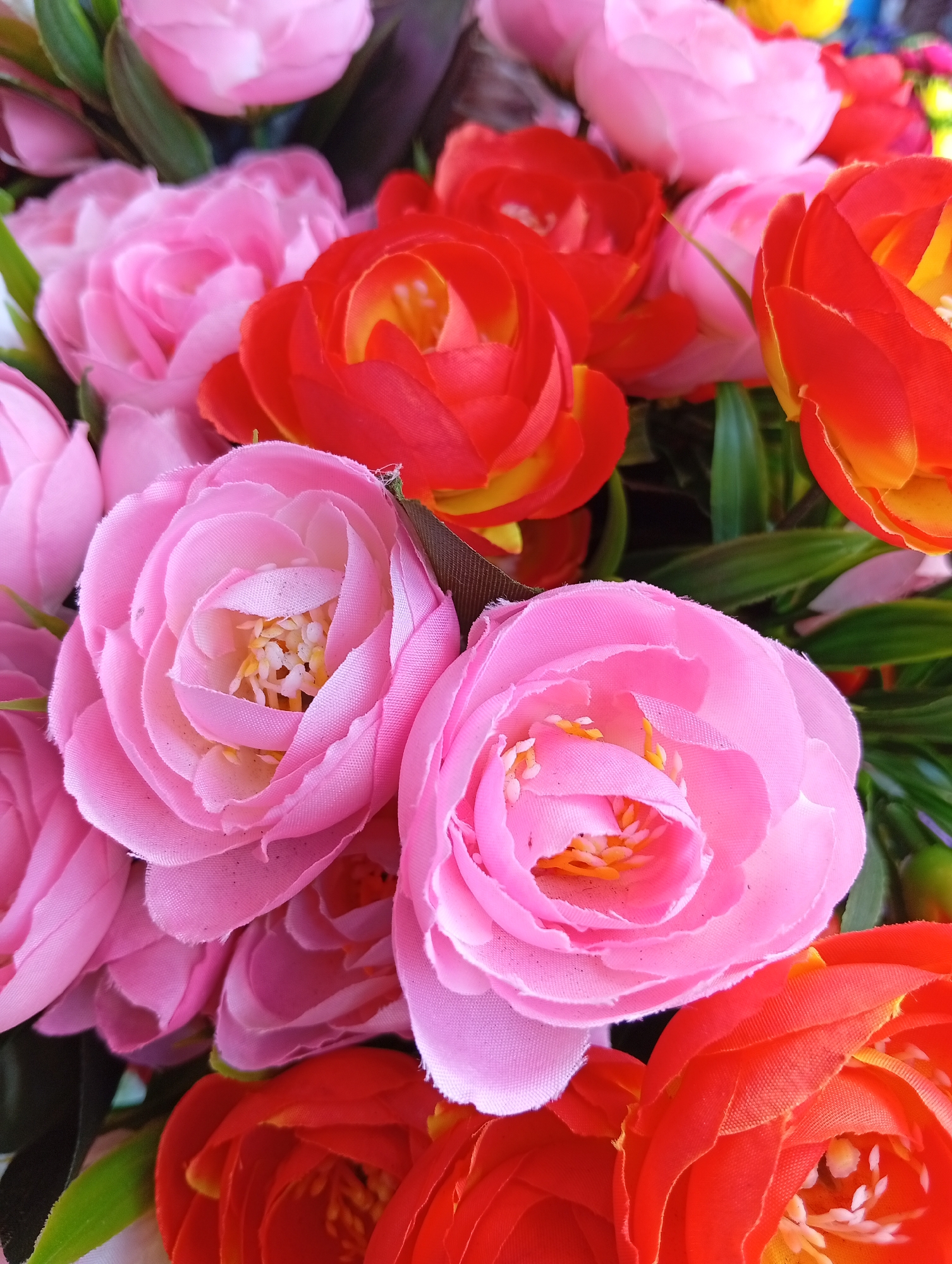 The image shows a close-up of a bunch of artificial flowers in shades of pink and red. The flowers are densely packed together, filling the frame. The composition emphasizes the textures and colors of the synthetic petals. There is no evidence indicating that this image was taken in Yekaterinburg, Russia.