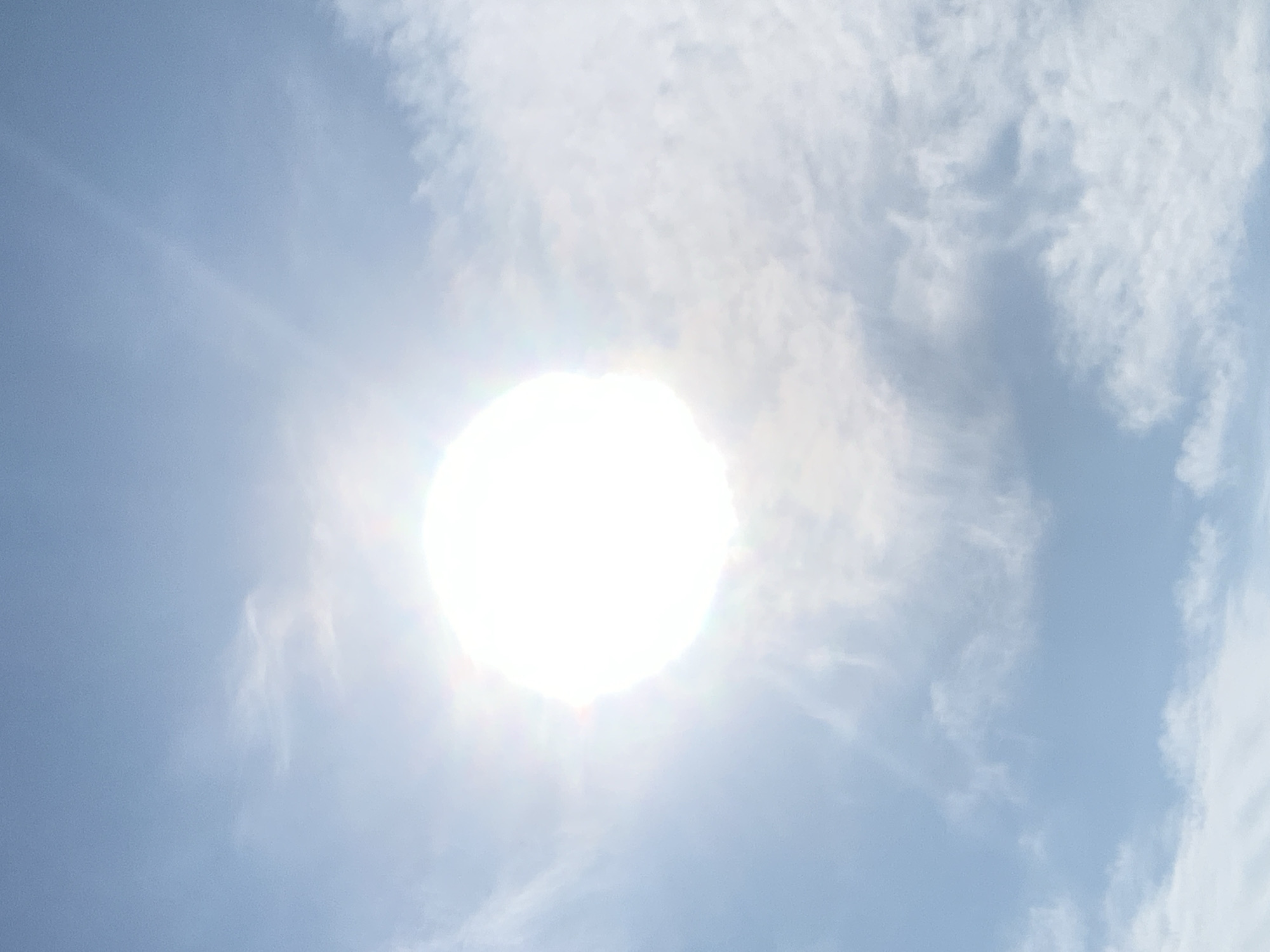 The image depicts a bright sun in a clear sky, with scattered clouds. There is no indication of the city of Kolomyia, Ukraine, or any specific environmental details that would allow for such a determination. The scene is solely of the sky and the sun, with no other objects or subjects present.