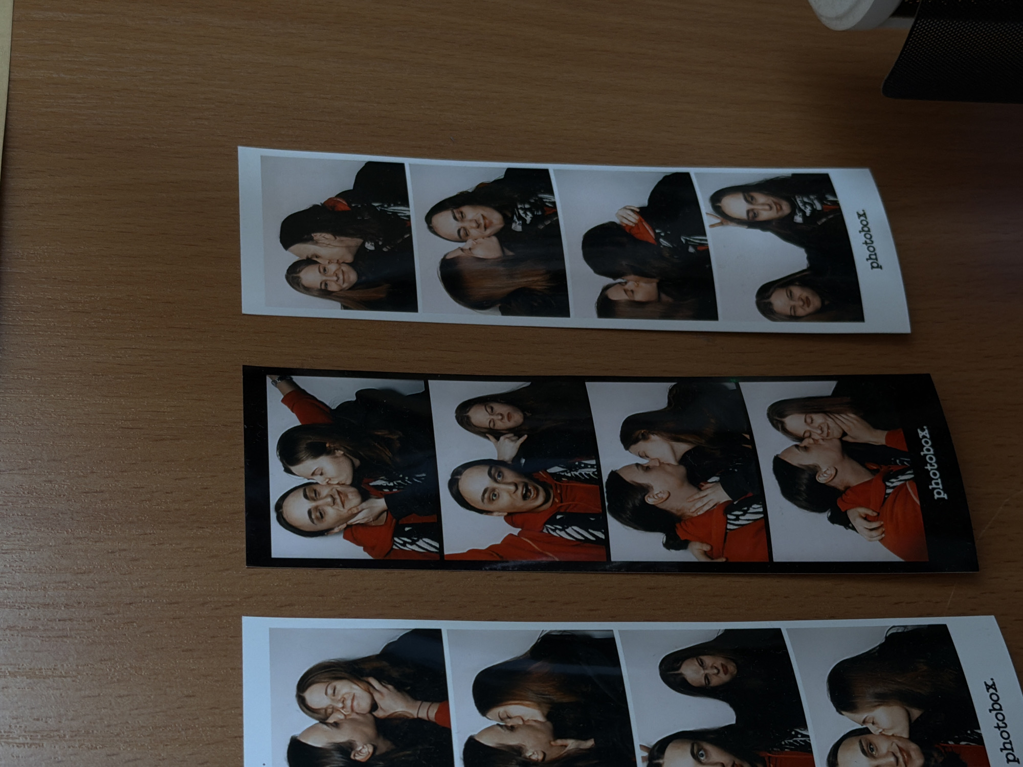 The image shows three photobooth strips lying on a wooden surface. Each strip contains four images of two young women. The women are embracing and kissing in various poses. The strips are labeled "photobox." The image does not show the city of Shul'gino, Russia, or provide any information to suggest that it was taken there.