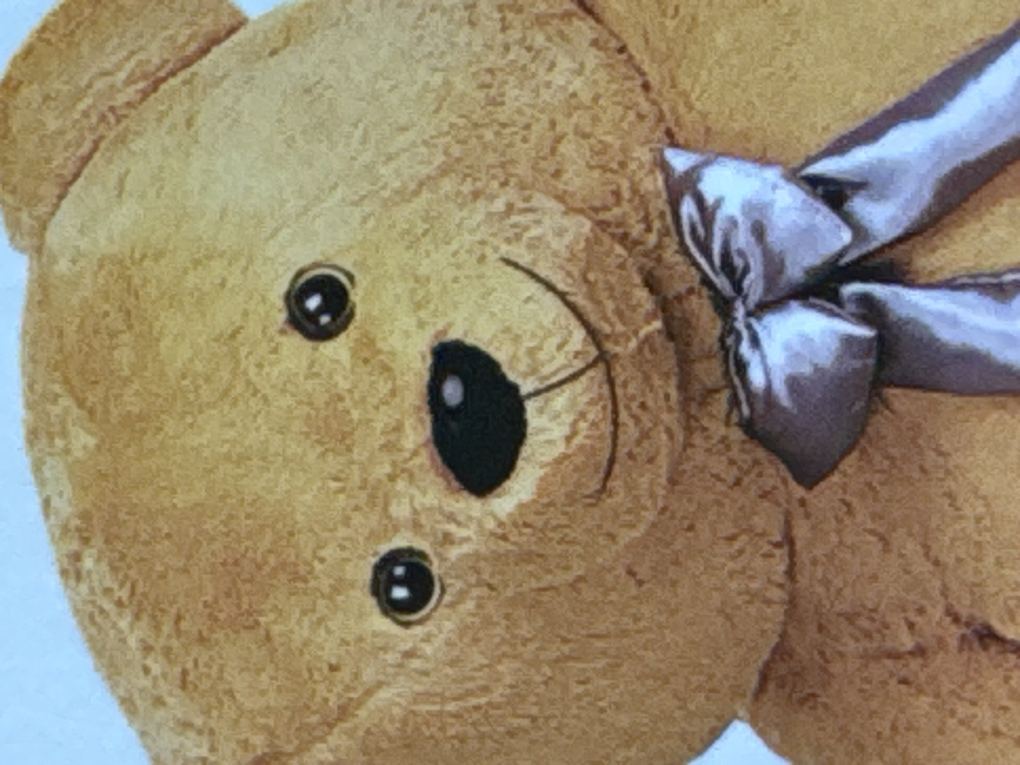 This is a close-up, waist-up, eye-level shot of a light brown teddy bear. The teddy bear is facing forward and is wearing a large, silver satin bow tied around its neck. The background is a solid, light blue color. The teddy bear's fur has a textured appearance. Its eyes are round and black with white highlights, and it has a black nose and a stitched smile. The image does not depict any specific location within the city of Яромінскі сельскі Савет, Belarus.