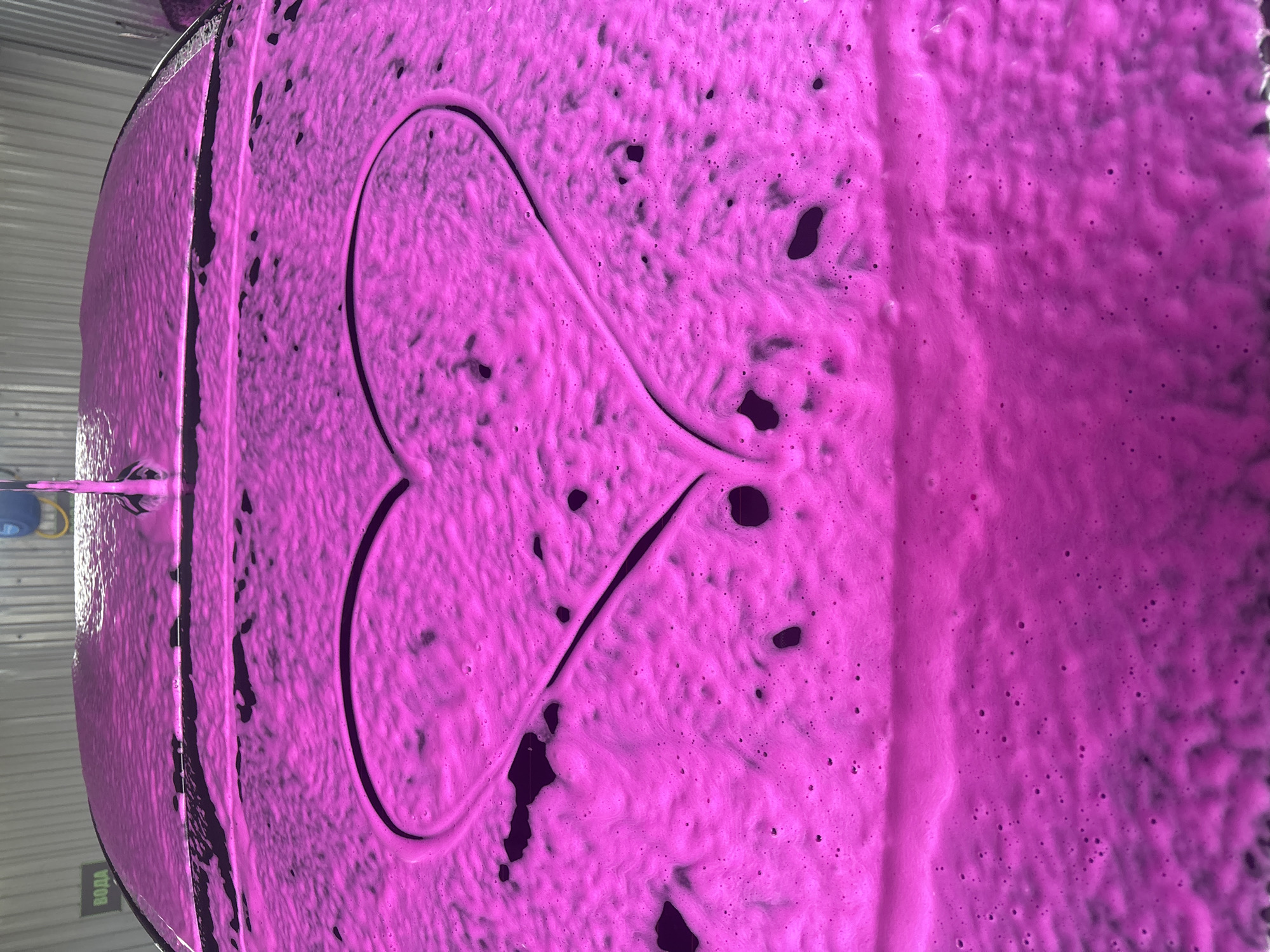 A vehicle is covered in pink soapy foam, on which a phallic shape has been drawn. The photograph appears to have been taken at a car wash facility, based on the presence of wash equipment. It is unclear if the image location in the city of Chaikovsky, Russia is accurate.