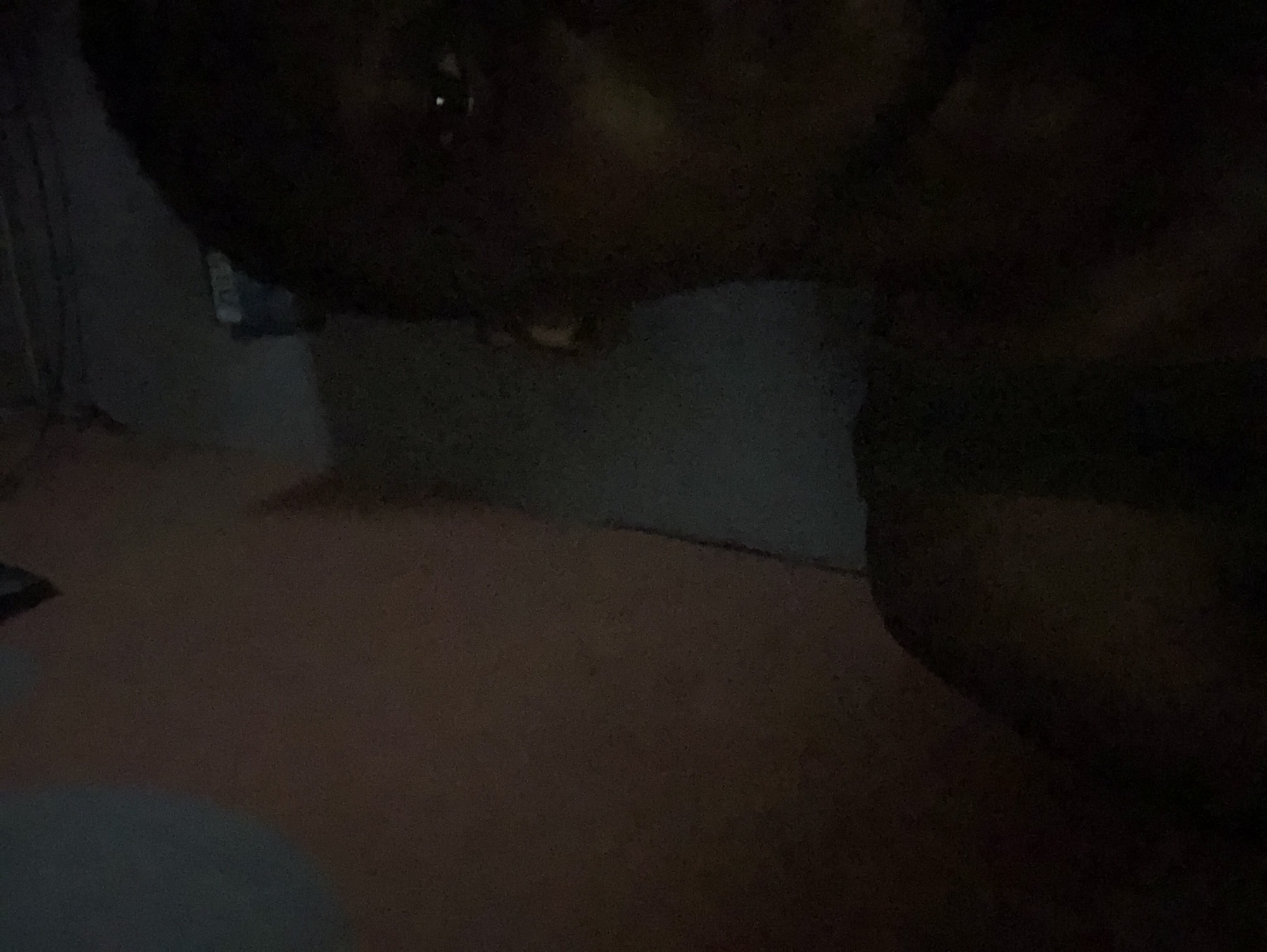 The image is very dark and difficult to discern. A person's face is partially visible in the upper part of the image, with only one eye clearly distinguishable. Below the face, there is a wall and what appears to be a carpeted floor. The location is Unknown, Unknown.