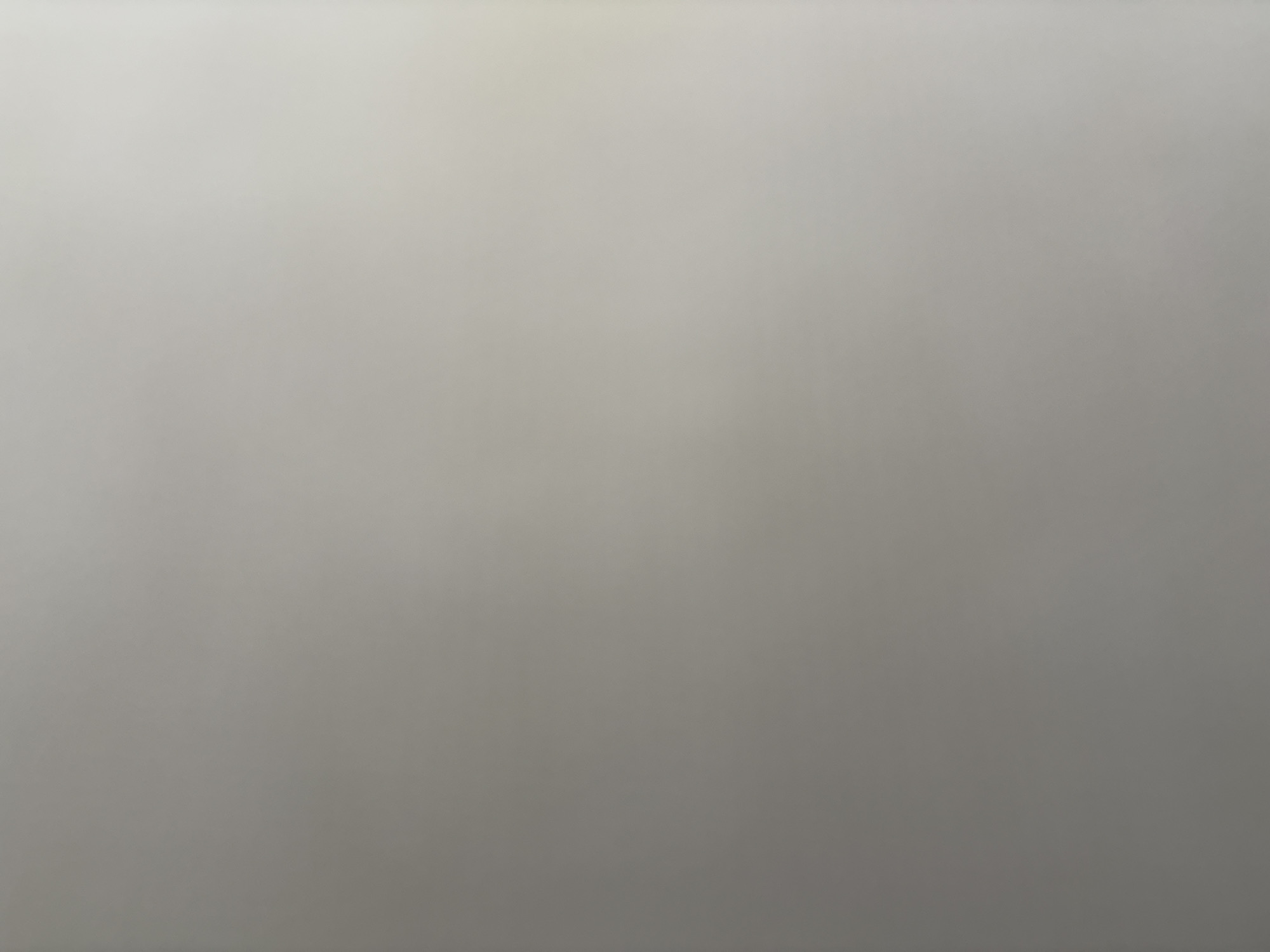 The image is a close-up, abstract shot of a neutral-colored surface, likely fabric or paper, with subtle variations in tone and texture. There are no discernible subjects, objects, scene, setting, or activity taking place. The lighting appears diffused, creating a soft gradient across the image, with areas of slightly brighter and darker tones that suggest subtle undulations or a very fine texture. No time of day, weather, location cues, or emotions can be inferred. There is no visible text in the image.