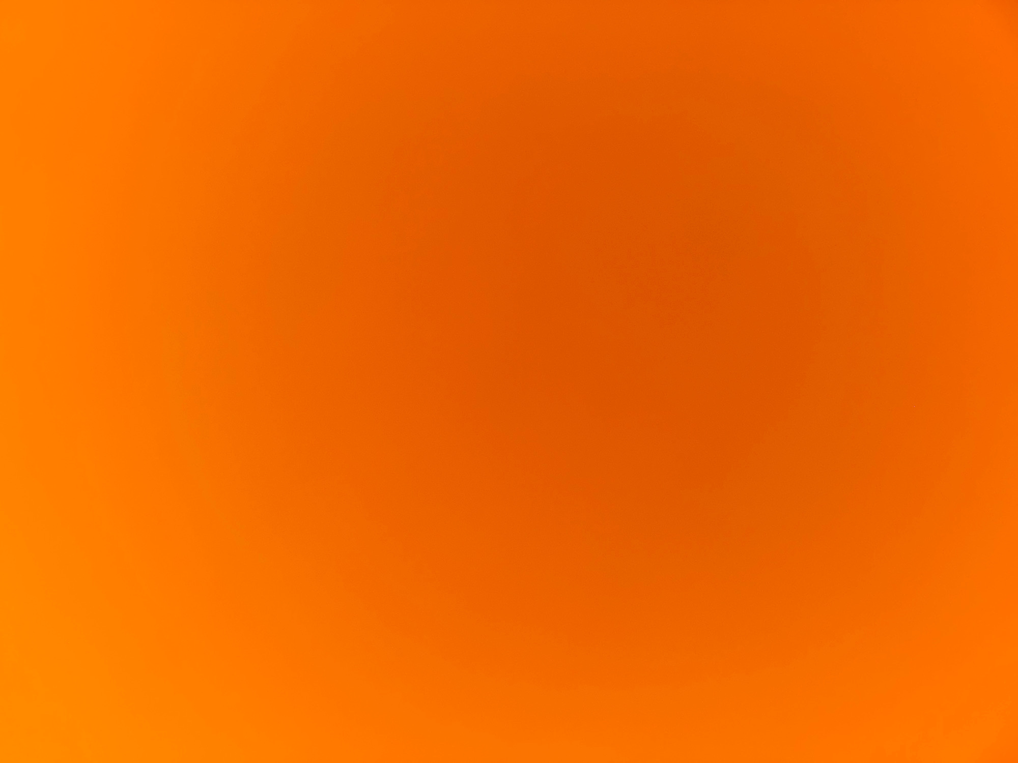 The image is an abstract, out-of-focus shot of a vibrant orange surface. There are no discernible objects, people, or environmental features. The lighting appears to be diffused, creating a soft gradient effect with a slightly brighter area towards the bottom left. There is no identifiable location within Ko Samui District, Thailand, or any other place.