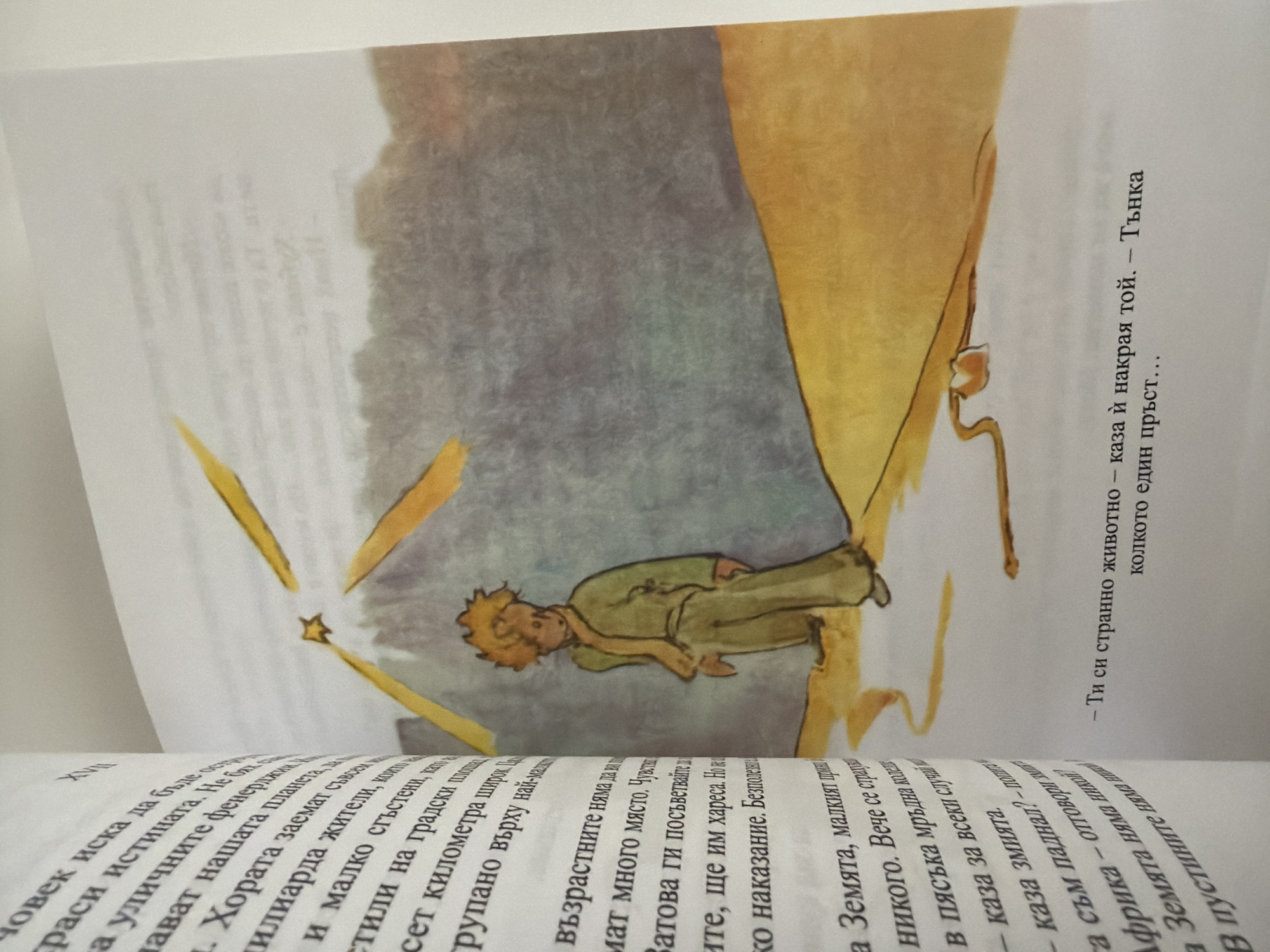 The image shows an open book with text and an illustration. The illustration is of a young boy with blond hair, wearing a green jacket and pants, standing on an orange, sandy surface. He appears to be looking up at yellow streaks, possibly shooting stars or light trails, against a greyish-purple sky. To the left of the illustration is a page with text in Bulgarian. The text discusses people, planets, and inhabitants. The book is positioned on a white surface, and a shadow is cast on the right side of the page, indicating the light source. There is no visible indication of the city of Pazardzhik, Bulgaria, within the image itself.