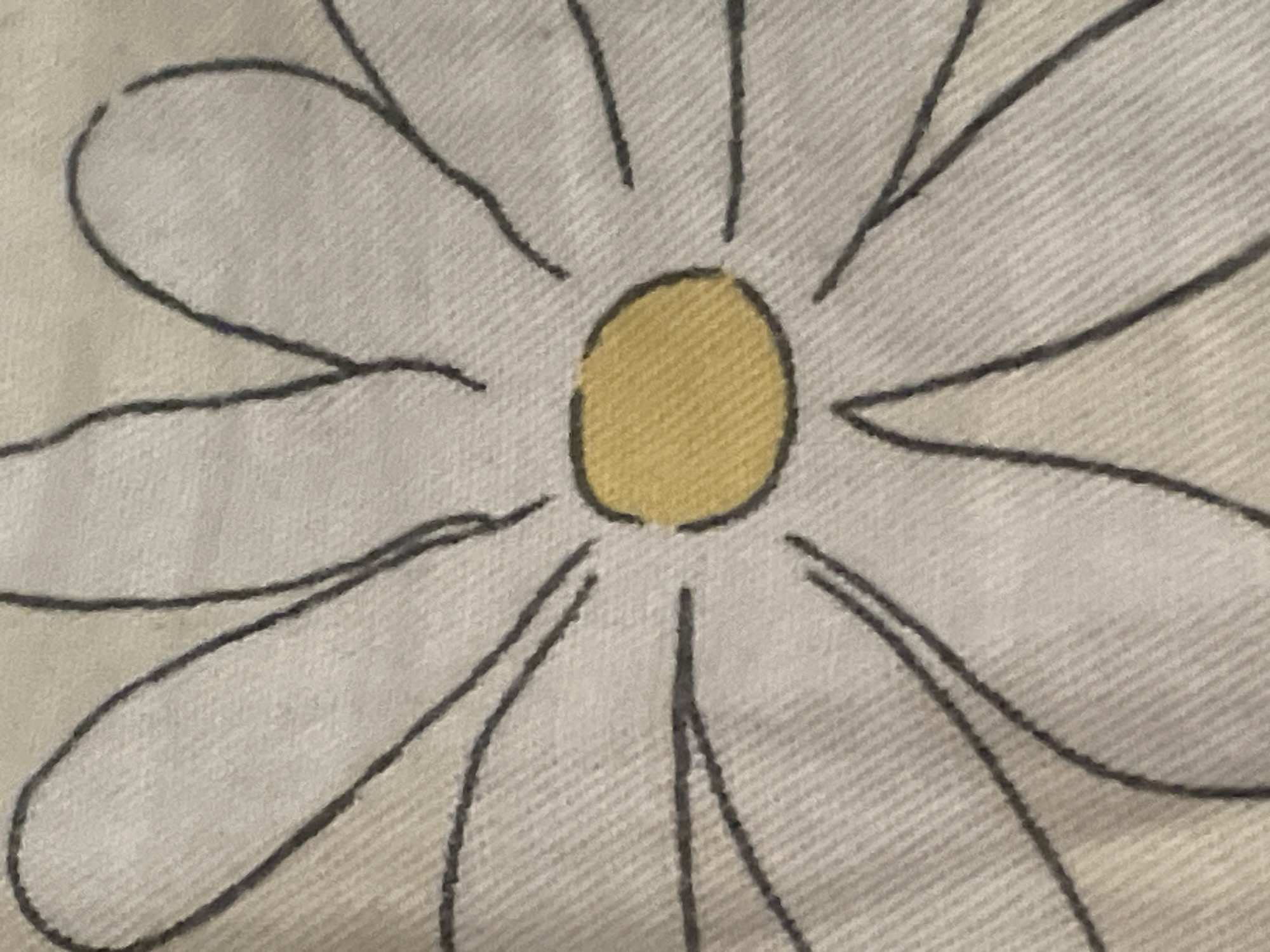 The image is a close-up, top-down view of a daisy illustration on a textured fabric. The daisy has white petals outlined in black, and a yellow center. The fabric appears to be light-colored and has a visible weave. There is no indication of a specific location in Tashkent, Uzbekistan, or any people or actions.
