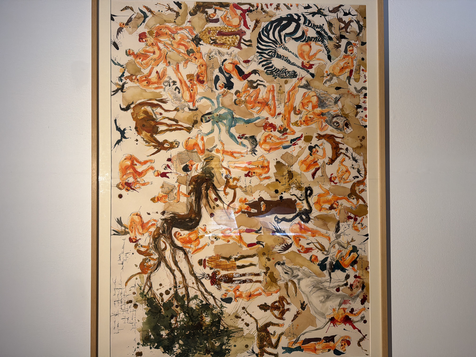 This is a framed artwork, likely a painting or drawing, featuring a chaotic and densely populated scene. The primary subjects are numerous nude and semi-nude figures in various poses, interspersed with animals such as a zebra, a horse, a fish, and monkeys. There are also depictions of what appear to be abstract forms, branches, and foliage. The style is loose and expressive, with watercolor and ink evident. The figures are rendered in warm, earthy tones, predominantly orange and brown, with some darker accents and washes.
The overall impression is one of disarray and movement, with figures seemingly falling, reaching, or interacting in an unclear narrative. Some figures are reading or holding objects, while others are intertwined or in dynamic poses. The composition is crowded, with elements overlapping and filling the entire space. There are splashes of ink and paint, adding to the sense of energy and perhaps turmoil.
Notable details include the presence of what looks like a snake, a fish with discernible scales, and the stylized black and white stripes of the zebra. The lower left portion of the artwork includes what appears to be handwritten text in cursive script, predominantly dark ink on a lighter background, which is difficult to decipher. The artwork is framed in a simple wooden frame. The background against which the artwork is displayed appears to be a light-colored wall. No specific time of day, weather, or strong emotional cues beyond a general sense of activity are immediately apparent, but the imagery could be interpreted as symbolic or allegorical. The location context of La Cuesta, Spain, provides a geographical setting but no specific visual cues within the artwork itself.