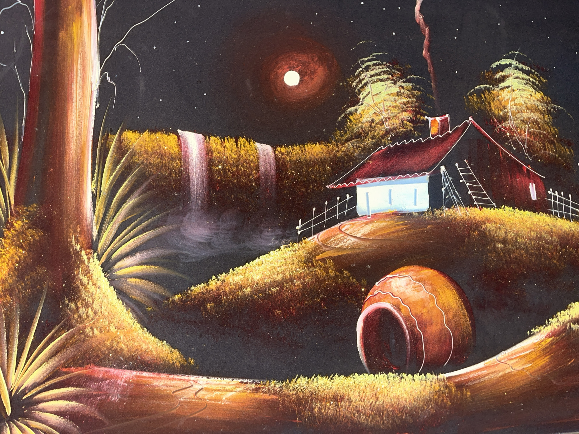 This painting depicts a nocturnal landscape. A prominent, bright white moon surrounded by a red halo illuminates a dark sky speckled with numerous small white stars. A jagged, reddish streak, possibly lightning, descends from the top-center towards the distant house. In the foreground, a substantial tree trunk, rendered in reddish-brown with golden-yellow highlights, occupies the left side, with sparse white branches extending upwards. Golden-yellow foliage extends from its base across the immediate foreground. In the midground, two luminous white and pink waterfalls cascade down a vibrant golden-yellow cliff, creating a misty base. To the right of the waterfalls, a small house with a steep, dark red gable roof and white walls sits on a grassy hill. A distinct orange glow emanates from its chimney, and a white ladder leans against the right side of the structure. A white picket fence is partially visible to the right of the house. In the lower right foreground, a large, reddish-orange ceramic pot or urn lies on its side amidst glowing golden-yellow grass. A subtle path with wavy lines is visible nearby. The background features rolling hills covered in bright golden-yellow foliage. The entire scene is set in the city of Santa Ana, Venezuela.