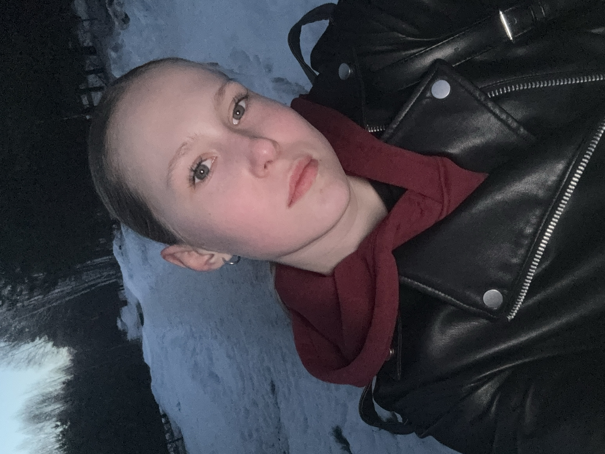 A person is wearing a black leather jacket and a red scarf. The background includes snow and trees, and the photo appears to be taken outdoors in Chaikovsky, Russia.