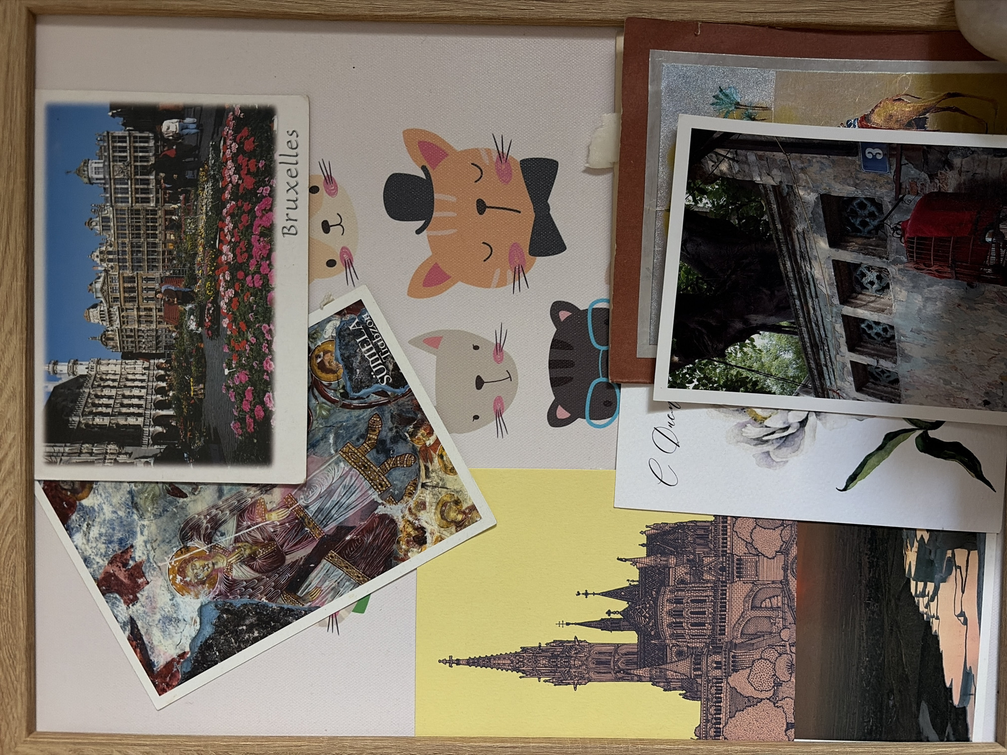 The image shows a framed collage of postcards and other images. One postcard features the Grand Place in Brussels with the word "Bruxelles" printed on it. Another image has a repeating pattern of cartoon cats with varying accessories like a top hat and glasses. There's a postcard with religious iconography and a building depicted in a detailed architectural sketch against a yellow background. An image of a building with a red object hanging outside appears to have a number "3" above the object. The postcards are layered and overlapping within the frame.