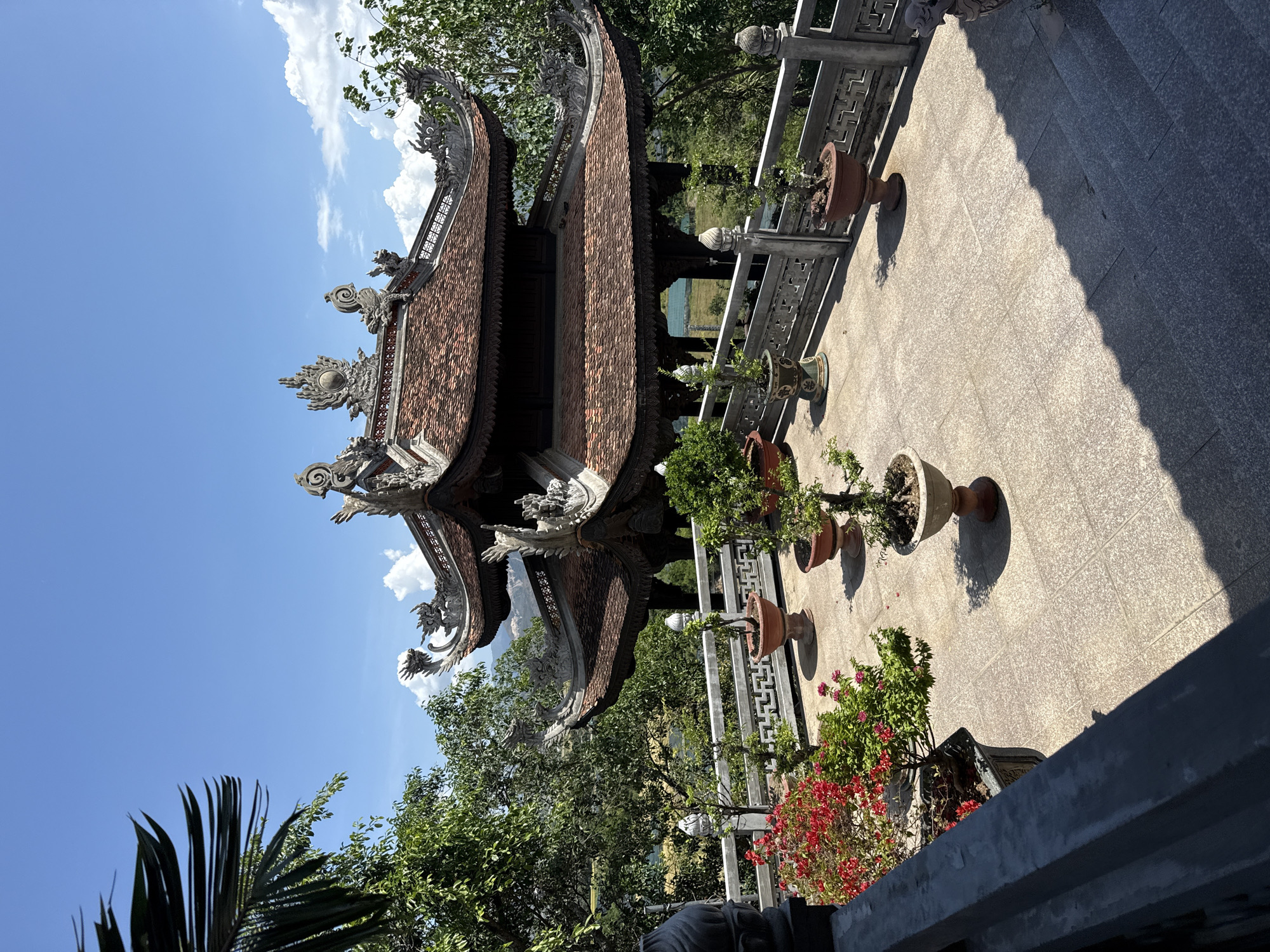 The image depicts a traditional Vietnamese pagoda or temple structure. The pagoda has a multi-tiered roof with ornate carvings and embellishments, particularly at the edges and corners of the roof. The roof tiles appear to be reddish-brown.
The pagoda is surrounded by trees and greenery. A paved area with potted plants is visible in the foreground, along with a stone balustrade.
Based on the provided information, the location is Tay Nha Trang Ward, Vietnam.