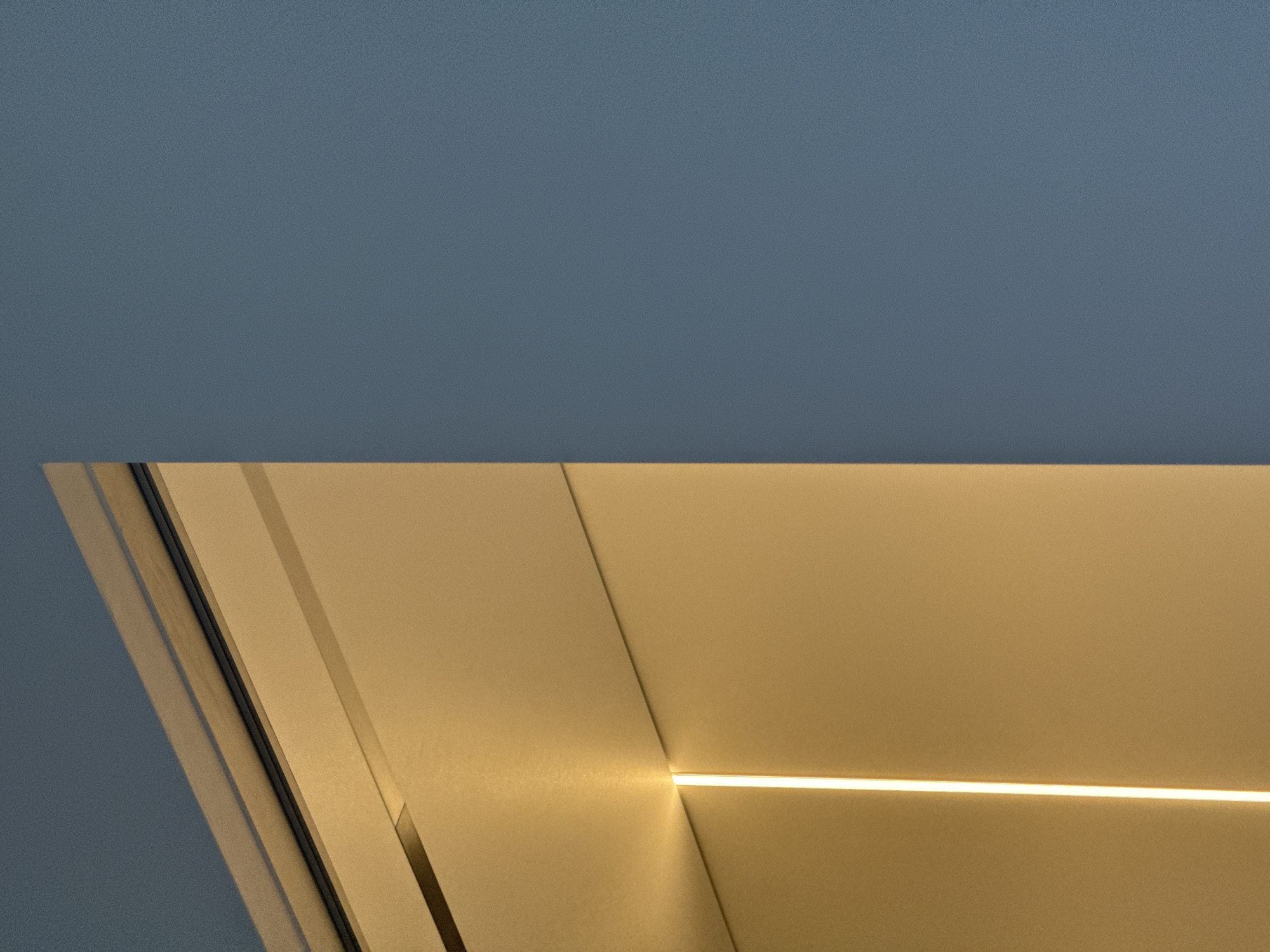 A low-angle, upward-looking photograph shows the intersection of a blue ceiling with beige wall panels featuring recessed linear lighting. The bottom left corner reveals an angled corner element, suggesting an architectural detail. No people, objects, or actions are visible. The image's location is Perm, Russia.