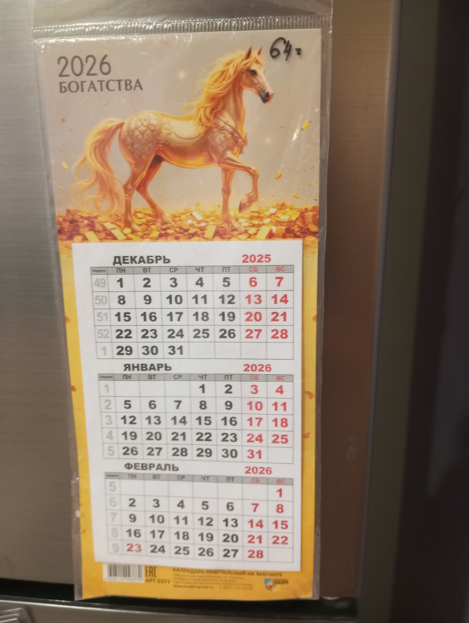 The image displays a calendar page for the year 2026, featuring an illustration of a golden horse surrounded by gold bars and coins, symbolizing prosperity. The calendar shows the months of December 2025, January 2026, and February 2026. The text on the calendar is in Russian, with "2026 БОГАТСТВА" at the top, meaning "2026 Wealth". The calendar is enclosed in plastic packaging. The lower part of the image shows an "EAC" certification mark and text that includes "КАЛЕНДАРЬ КВАртальный НА МАГНИТЕ", indicating a quarterly magnetic calendar. The overall scene suggests the calendar is affixed to a metallic surface, likely a refrigerator door, given the magnetic calendar description. There are no people or specific landmarks visible that would indicate a precise location within Verkhnyaya Pyshma, Russia.
