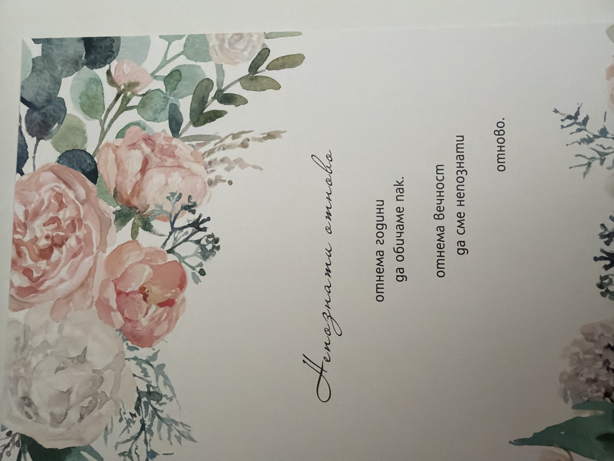 The image shows a printed card with a watercolor floral design. At the top, a border of pink and white roses with green leaves and eucalyptus branches frames the card. Below the floral design, in a script font, are the words "Непознати отново". Underneath this, in a standard font, are four lines of text. The first two lines read "отнема години" and "да обичаме пак.". The next two lines read "отнема вечност" and "да сме непознати". Finally, centered at the bottom of the text block, is the word "отново.". The bottom of the card also features a watercolor floral design with pink and white flowers and green foliage. The location of this card within the city of Pazardzhik, Bulgaria is not determinable from the image.