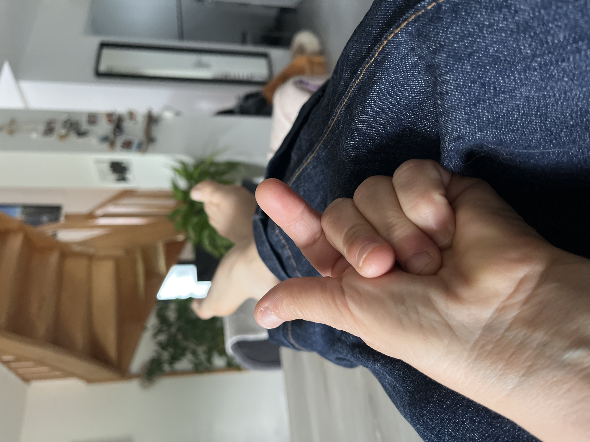 A person wearing denim jeans is seated indoors. A hand is visible, and bare feet are also visible. Stairs are visible in the background, along with a plant. The location is possibly a residence in Chambœuf, France based on the original query.