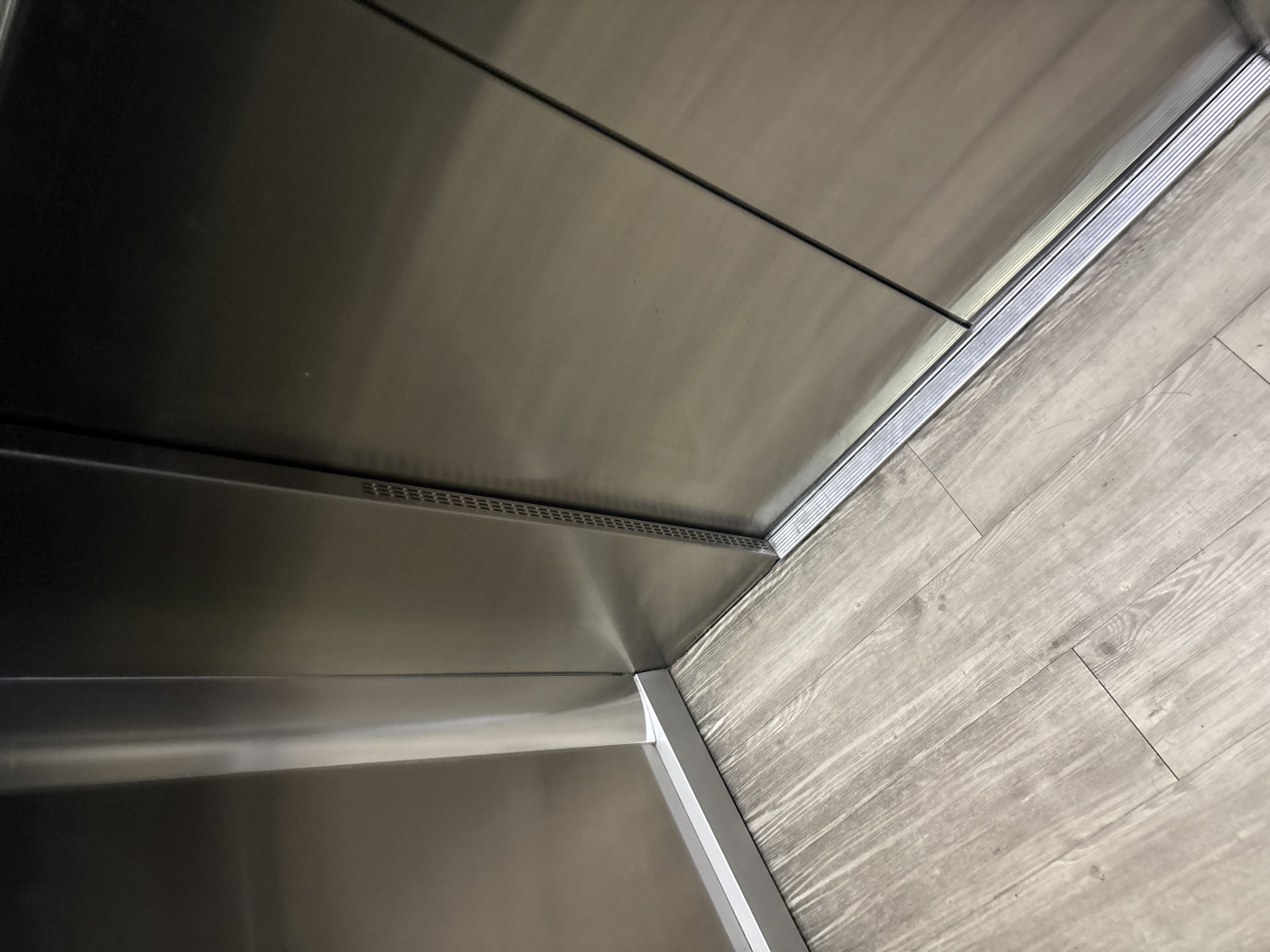 The image presents an interior shot, primarily featuring metallic surfaces and what appears to be light-colored wood-patterned flooring. The metallic surfaces are likely stainless steel, given their smooth, reflective quality. One section contains small perforations. The flooring material is reminiscent of wood flooring, with linear patterns suggesting planks. The scene's location within Mexico City, Mexico, cannot be determined from visual elements.