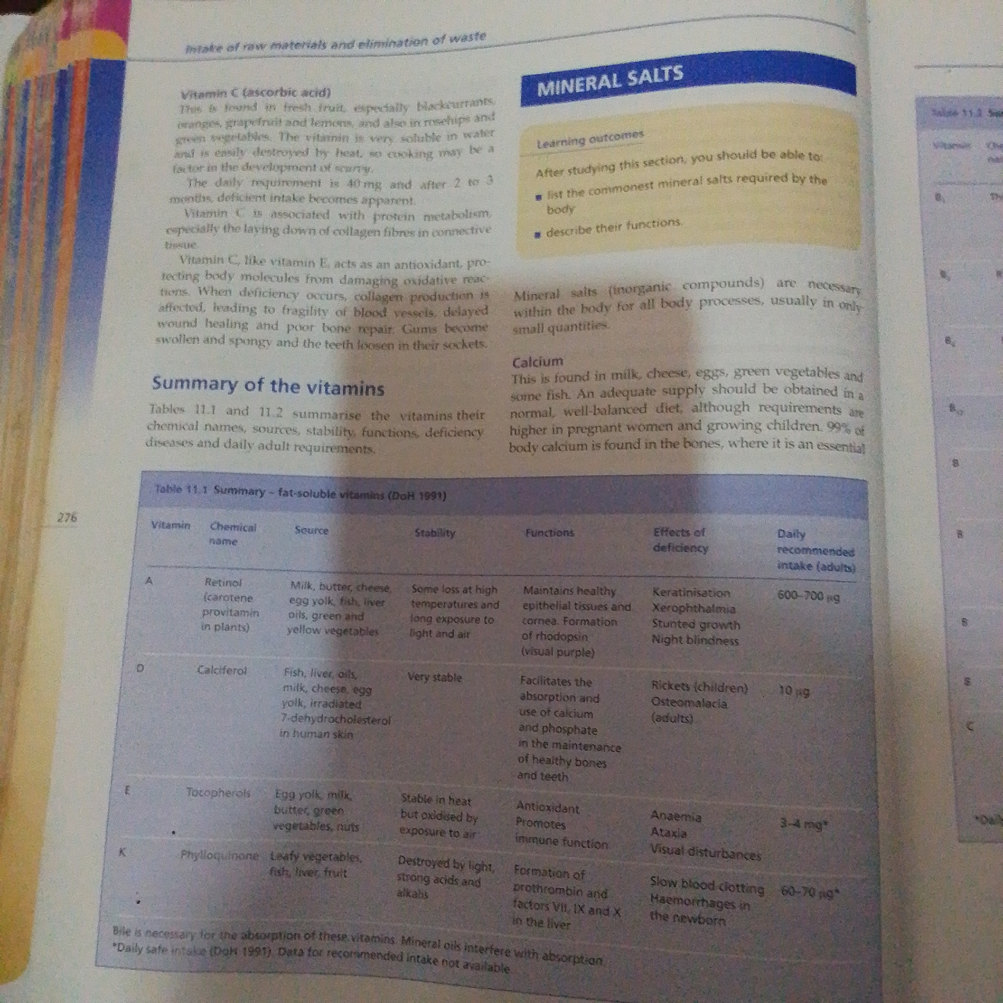 The image shows a page from a textbook or reference book discussing vitamins and mineral salts. The text is in English and includes headings such as "Intake of raw materials and elimination of waste," "MINERAL SALTS," and "Summary of the vitamins." There is also a table titled "Table 11.1 Summary - fat-soluble vitamins." The content focuses on the sources, functions, and deficiency effects of various vitamins, as well as introductory information about mineral salts and calcium. The image appears to be a scanned or photographed page, with some areas slightly blurry. There is no information in the image that relates to the city of Jalingo, Nigeria.