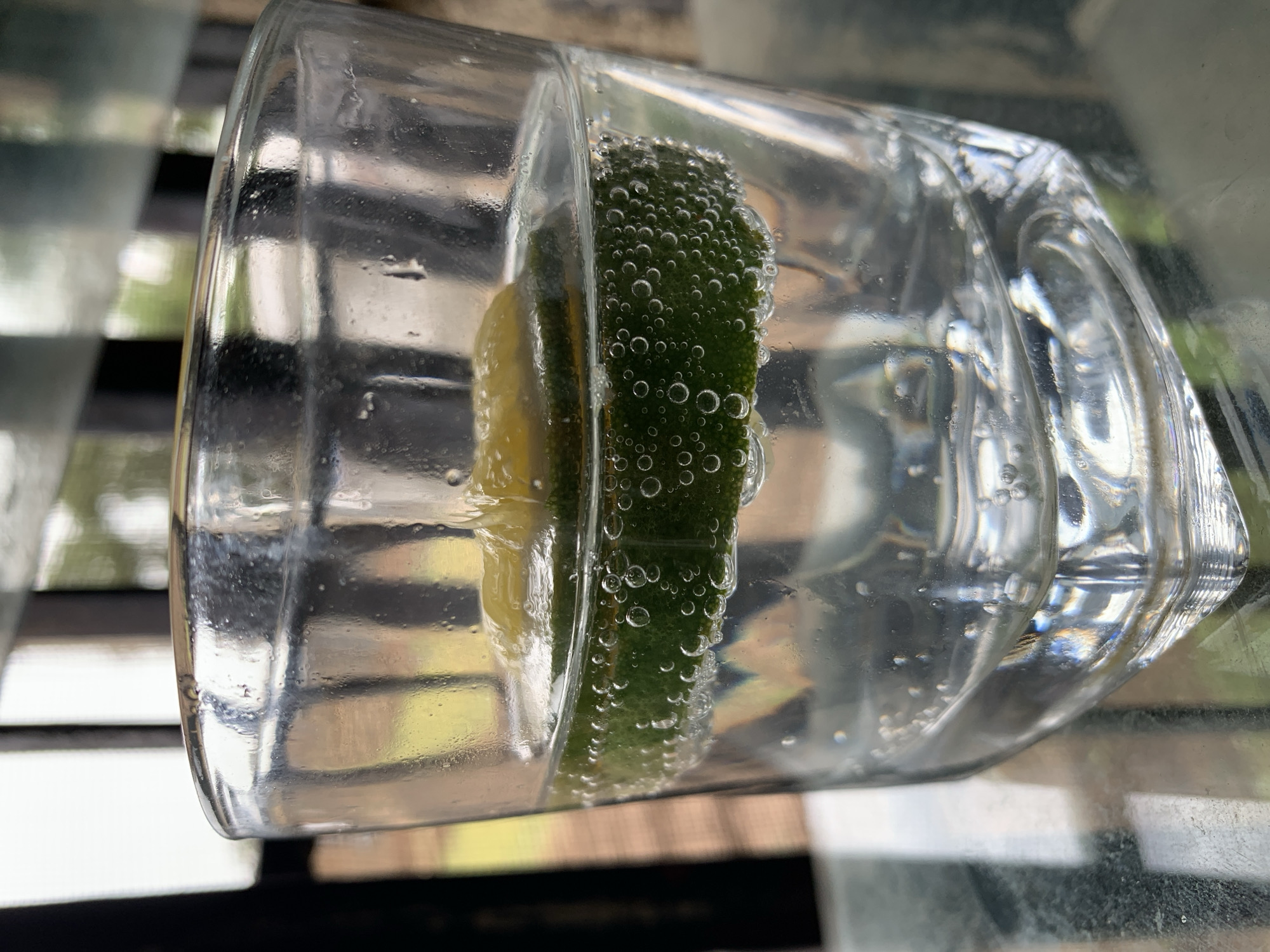 A glass of water with a slice of lime is on a surface. The lime has bubbles clinging to its surface. The background is blurry and indistinct. There is nothing that indicates this image was taken in Rafin Par, Nigeria.