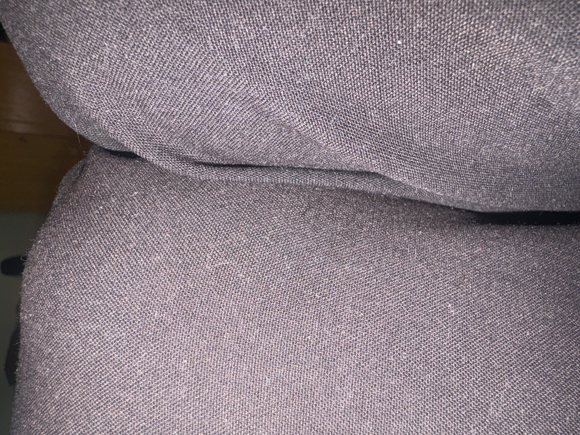 The image is a close-up, high-angle shot of dark-colored fabric, likely upholstery from a couch or chair. The texture of the fabric is visible, showing a woven pattern. The lighting is dim, suggesting an indoor environment. There is no discernible location in the city of Rivne, Ukraine, or any people or actions.