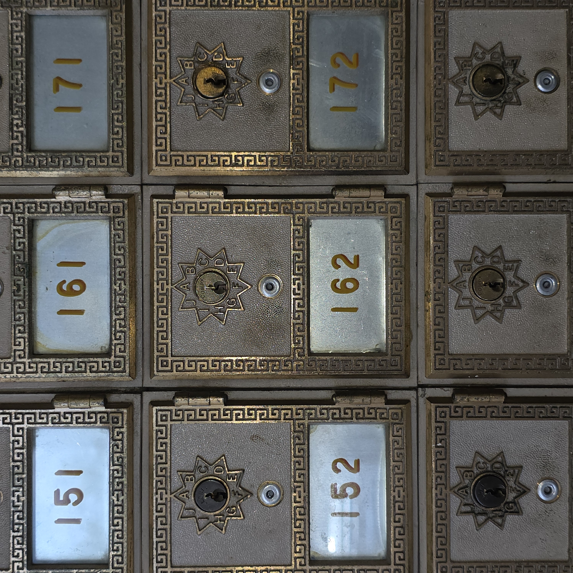 The image displays a grid of vintage metal post office boxes. The boxes are arranged in three columns and three rows, with the numbers 151, 161, and 171 visible in the top row, 152 and 162 visible in the middle row, and 172 visible in the bottom row. Each box features a metal door with a circular lock and a star-shaped emblem with letters around it. The overall aesthetic suggests an older, possibly historic, building. The location of this post office is identified as being in Beaverton, United States of America, though no specific street address or building name is provided.