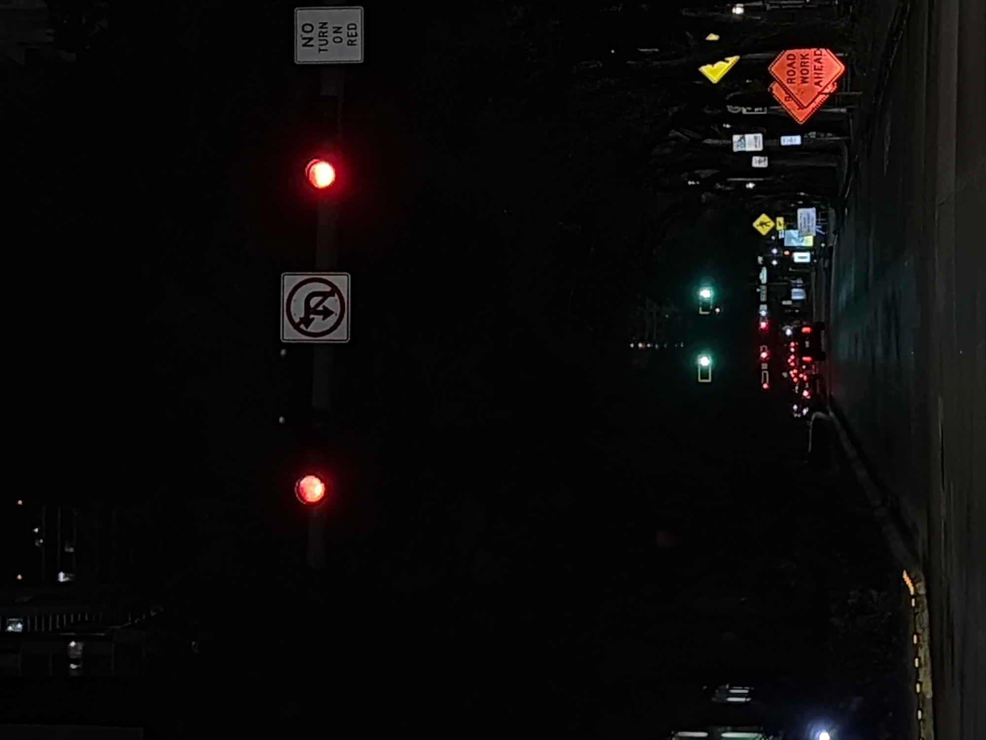 The image shows a street at night, with traffic lights displaying red signals. A "No Turn on Red" sign is visible. Road work ahead signs are also present. The location is likely in Miami, Florida, based on the request. Cars and traffic lights are seen further down the road. The scene appears to be a city street at night.