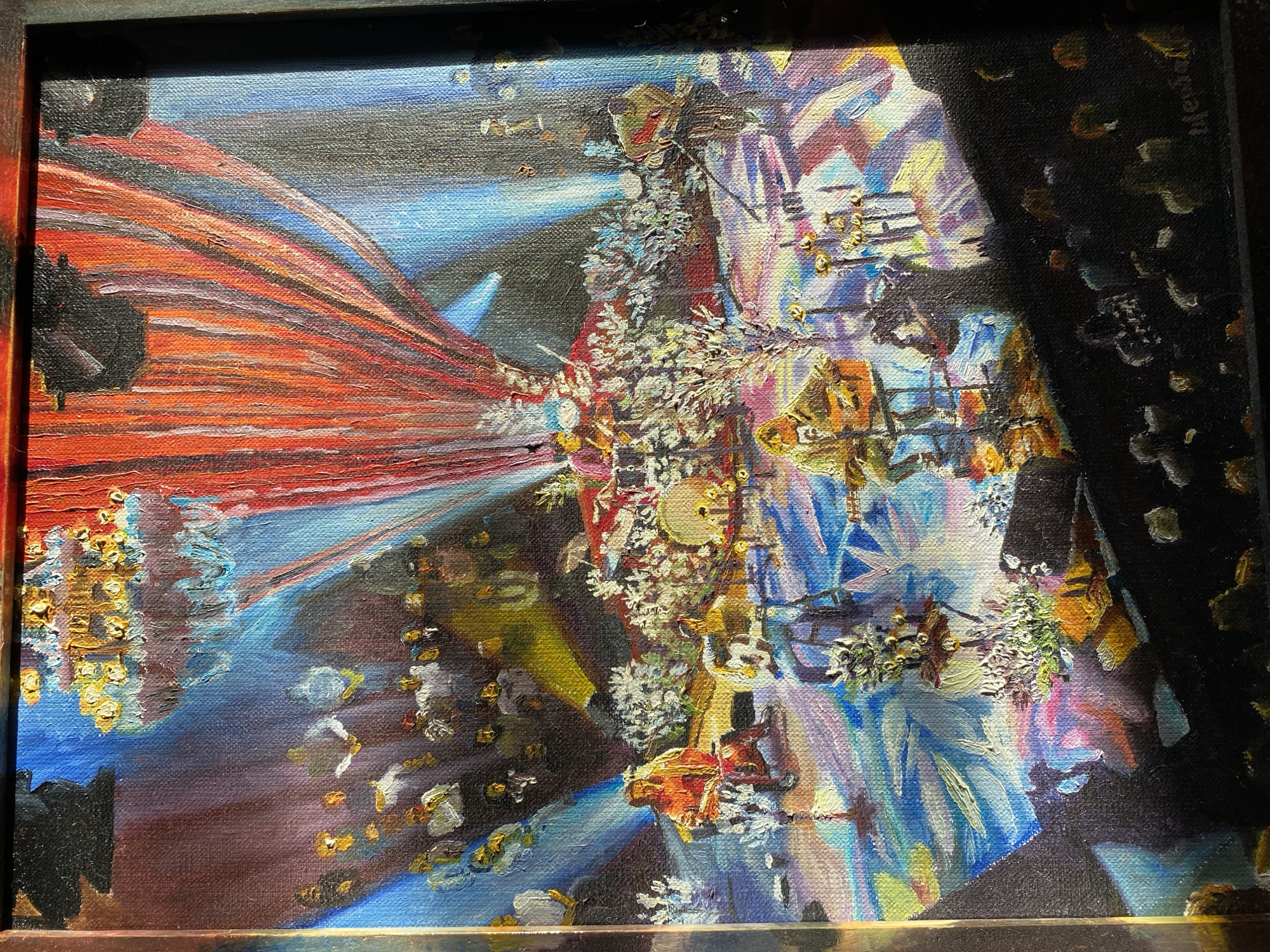 This is a close-up, horizontal, eye-level shot of an oil painting. The painting depicts an abstract, surreal scene rendered in vibrant, textured brushstrokes. Dominating the left side is a large, flowing form in shades of red and orange, suggesting drapery or a large wing, emanating from a dark, indistinct object. The center of the composition is a dense, swirling mass of white and light-colored elements, possibly floral or crystalline in texture, adorned with small, golden, circular accents. Behind this, and extending to the right, is a chaotic explosion of color, with bold strokes of blue, yellow, pink, and white forming abstract shapes that could be interpreted as architectural elements, light beams, or fragmented figures. Scattered throughout the scene are numerous small, gold-flecked or yellowish daubs, adding a sense of sparkle or distant lights. The right side of the painting is largely consumed by a deep, textured black area, with only hints of colored light breaking through, creating a dramatic contrast and a sense of depth. The overall impression is one of dynamism and illusion, possibly evoking a dreamlike or fantastical atmosphere. There is faint, illegible text written vertically in a darker color on the far right edge of the canvas, within the black area. The painting is framed by a dark border.