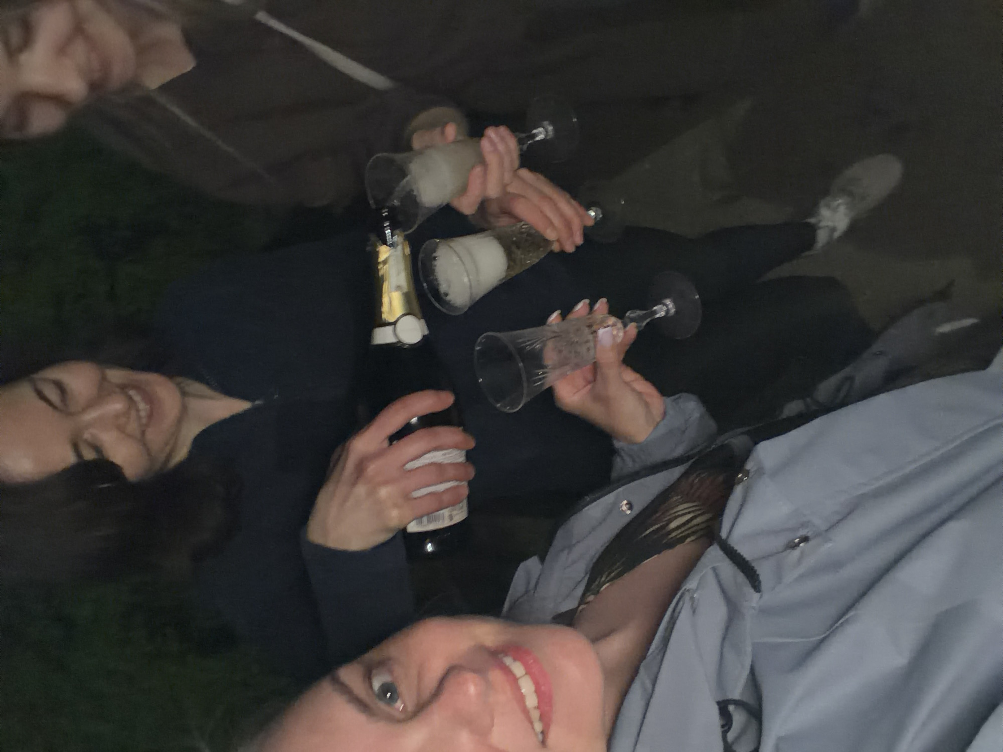 The image shows a group of people celebrating, possibly in an outdoor or dimly lit setting. Several individuals are holding champagne glasses filled with sparkling liquid, and at least one bottle of champagne is visible. The people appear to be interacting and enjoying themselves. The specific location in Votkinsk, Russia, cannot be determined from the visual information provided in the image. There is no way to ascertain the exact location from the image alone.
