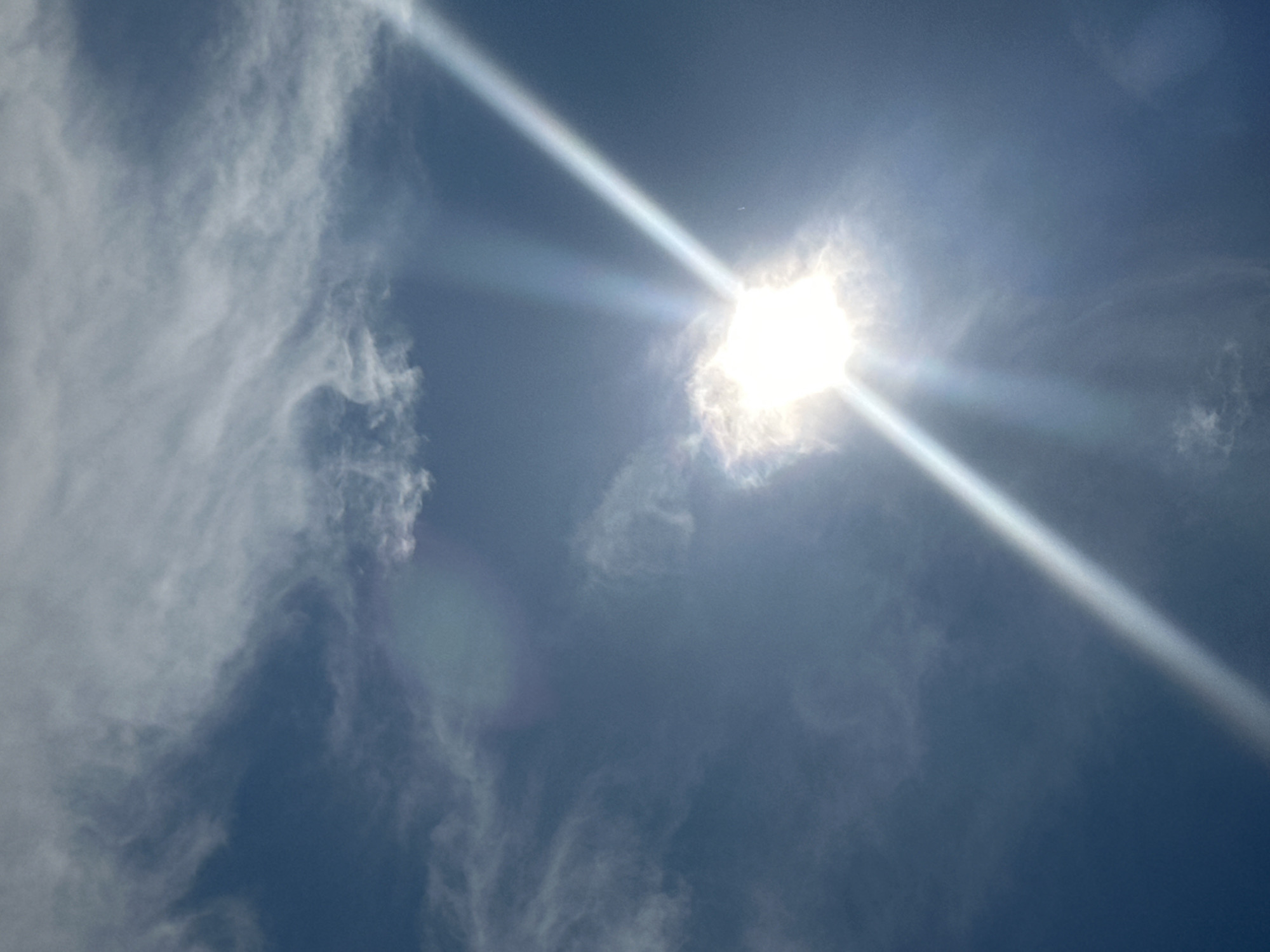 The image shows a bright sun with visible rays and a halo effect in a blue sky with scattered clouds. There is no information or visible content within the image that indicates the location in Podolsk, Russia, or the presence of any people, subjects, objects, or actions.