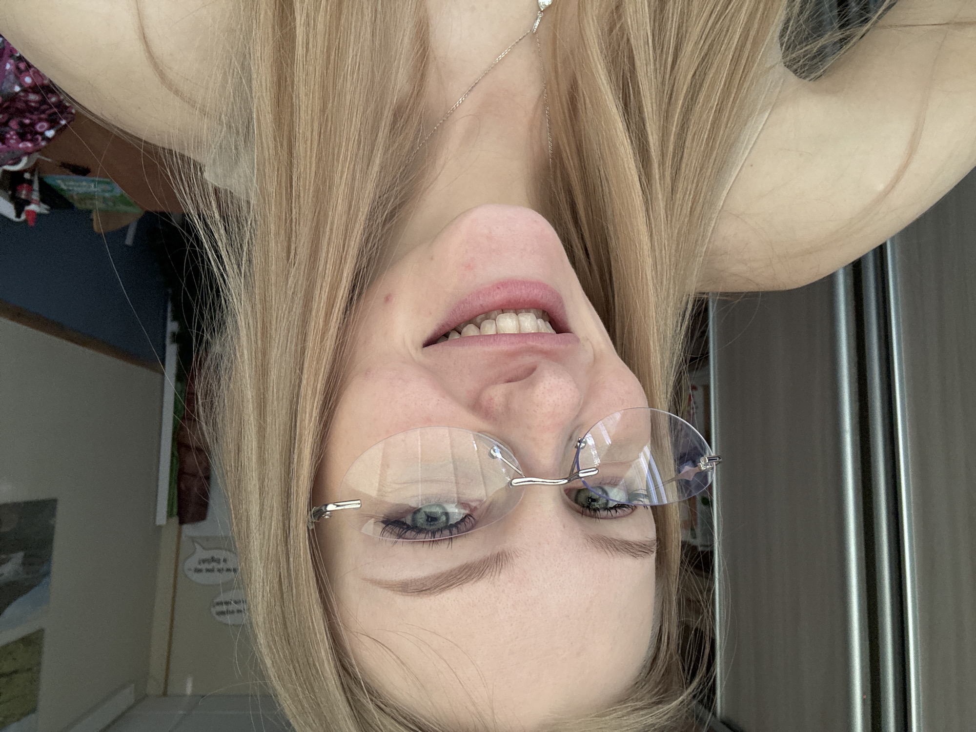 A selfie of a woman with blonde hair and glasses is oriented upside down. The location cannot be determined.