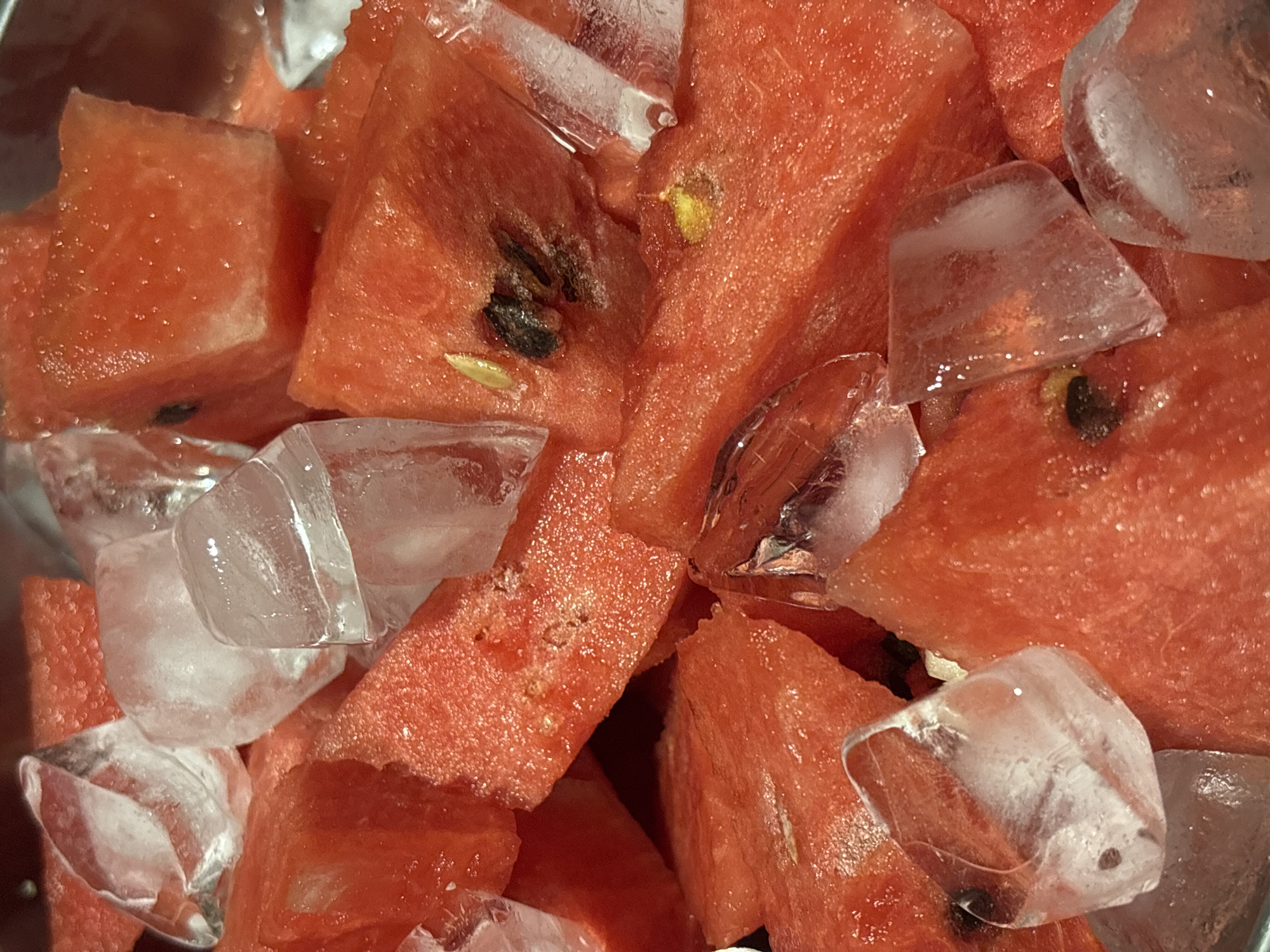 The image shows a close-up of cubed watermelon pieces mixed with ice cubes. The watermelon is a deep red color with scattered black and white seeds visible in some pieces. The ice cubes are clear and irregularly shaped, showing signs of melting. The overall impression is one of a refreshing, chilled snack. The image does not provide any information to determine if this image was taken in Choeng Thale, Thailand.
