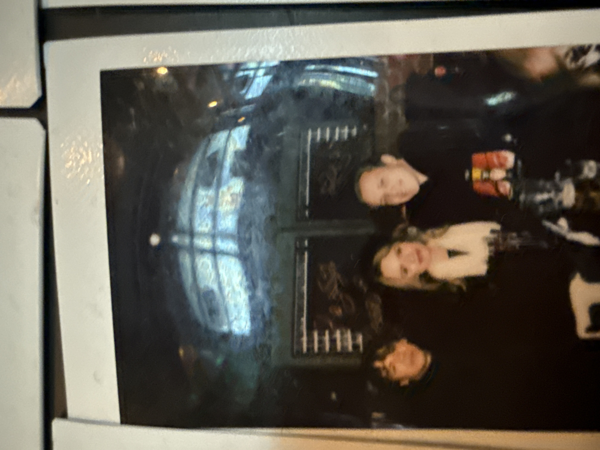 A photograph depicts three individuals, seemingly in an indoor setting. The backdrop suggests a location in Moscow, Russia, based on the presence of elements such as a possible metro station window. The individuals are posing in a manner that suggests a casual setting. Their clothing is predominantly dark. The photograph appears to be a casual snapshot.