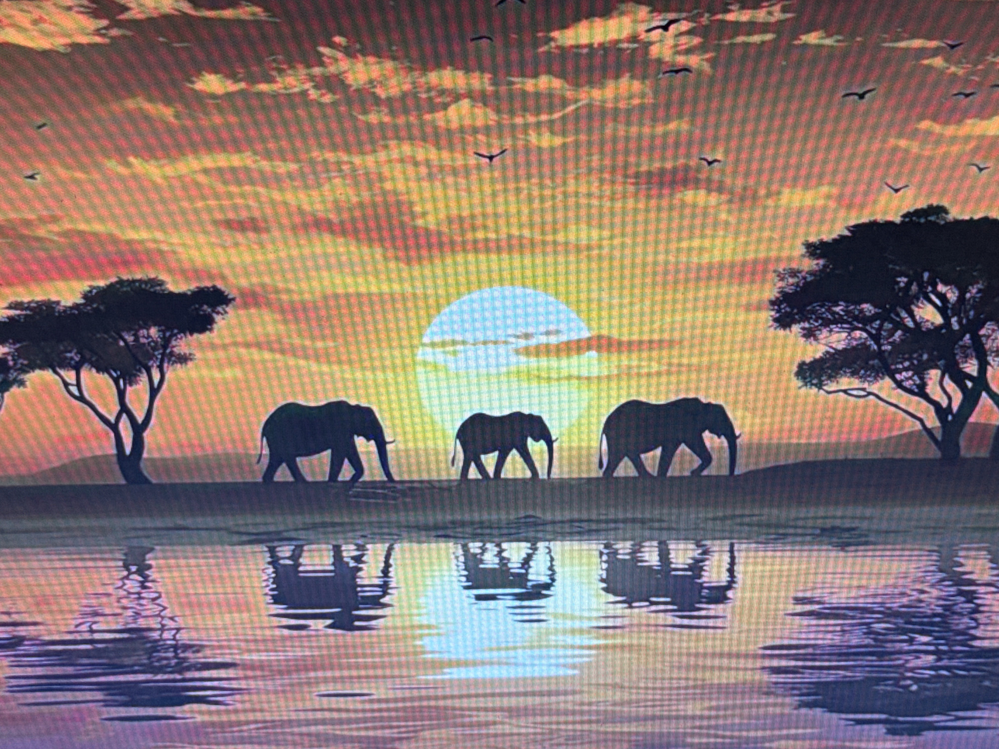 This image depicts a serene savanna sunset scene, with a large, pale sun dominating the horizon. The sky is ablaze with warm hues of orange, yellow, and pink, streaked with wispy clouds. Silhouetted against this vibrant backdrop are three adult elephants walking from left to right. They appear to be moving towards a body of water. To the left and right edges of the image, the silhouettes of acacia trees stand tall, characteristic of an African savanna. Below the elephants and trees is a reflective surface, likely water, mirroring the sky and the animals, creating a symmetrical composition. The water's surface is rippled, distorting the reflections slightly. The overall mood is peaceful and tranquil, evoking the quiet beauty of nature at dusk. There are no people, objects, visible text, or explicit location cues to suggest Pushkino, Russia, as the setting. The scene is characterized by the warm, golden light of a setting sun and the majestic presence of elephants in their natural habitat.