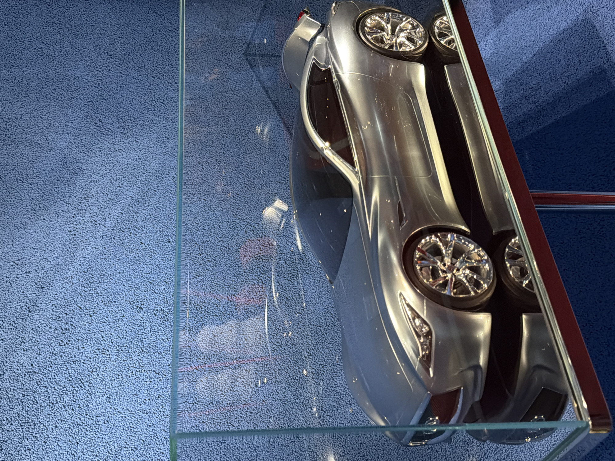 A silver toy car is displayed in a glass case in what appears to be an indoor setting. The background surface has a blue, textured appearance. The scene appears to be artificially lit. There is no indication of the location being in Jing'an District, China.